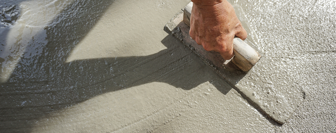 Close-up of a person's hand smoothing wet concrete with a trowel during construction.