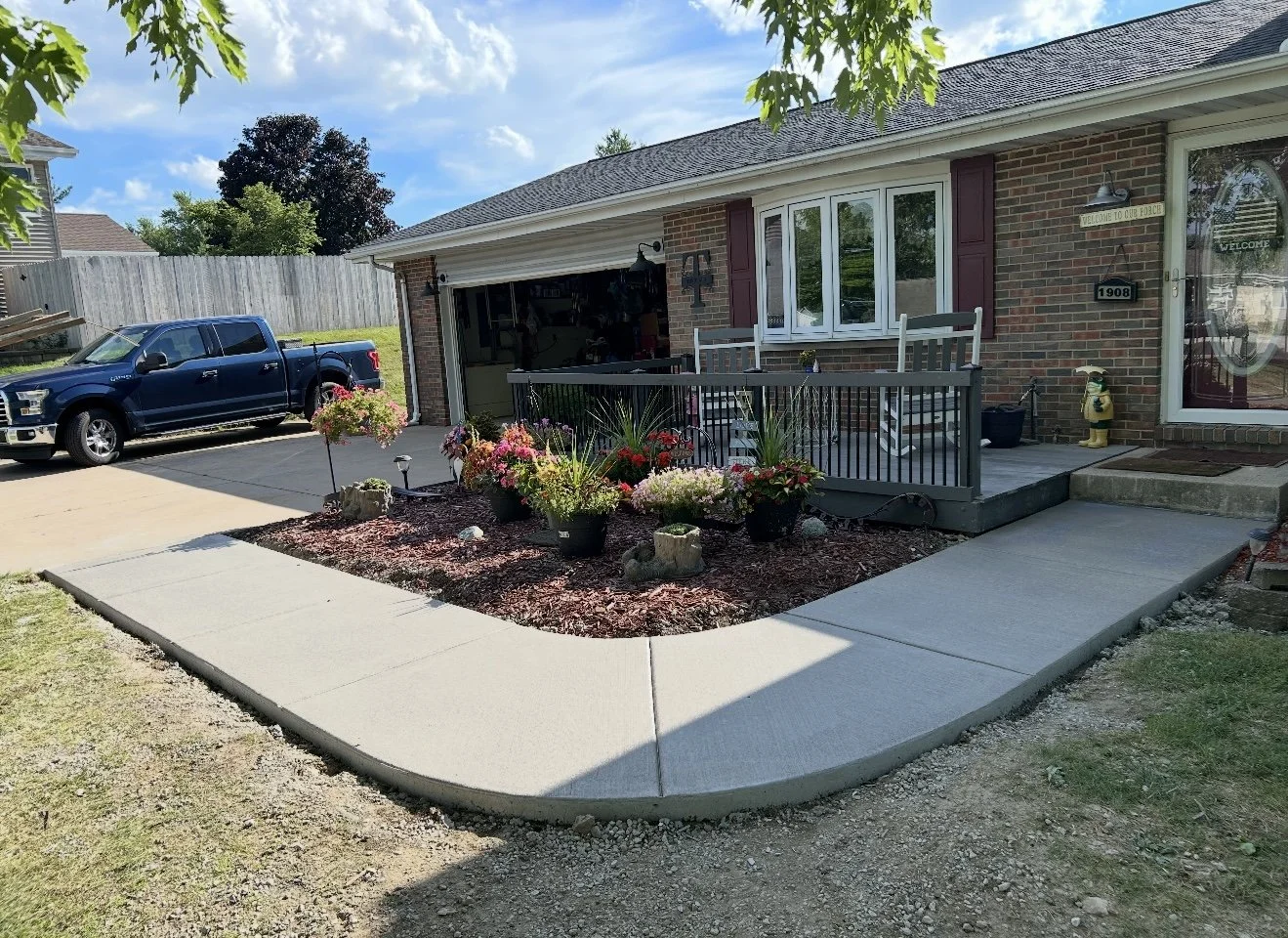 Front yard with a curved sidewalk, flower bed with colorful flowers, and a house with a brick wall and front porch. A blue truck is parked in the driveway.