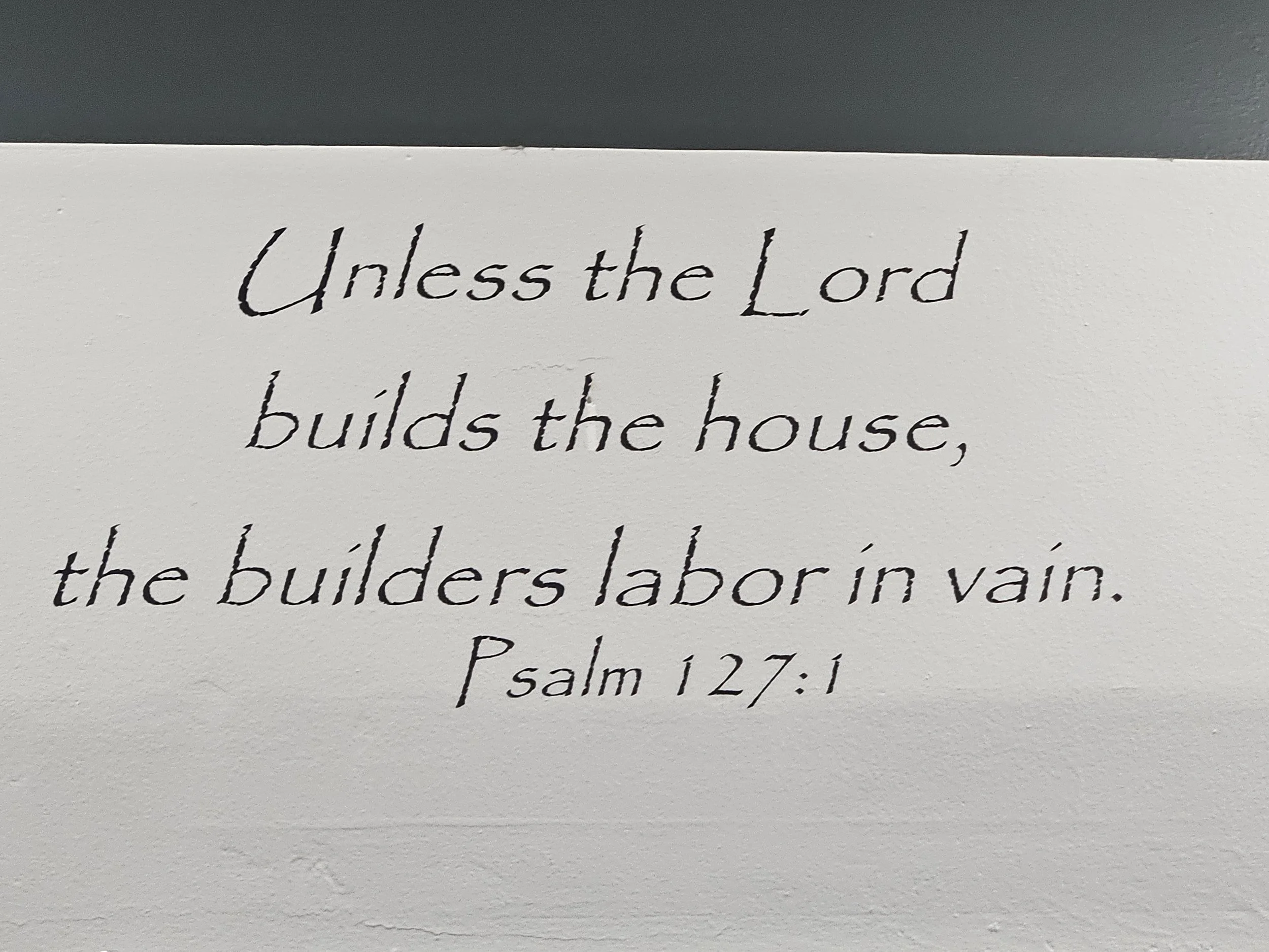 A framed quote on a wall that reads, 'Unless the Lord builds the house, the builders labor in vain. Psalm 127:1'.