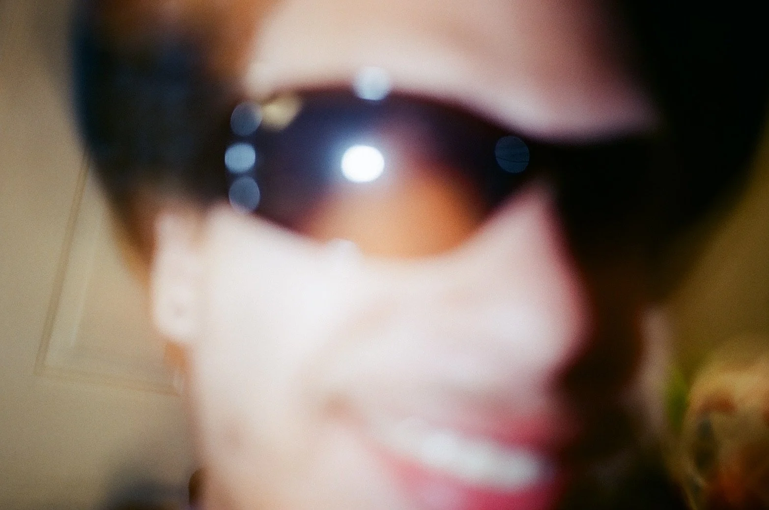 Close-up of a person's face with sunglasses reflecting bright lights, with their mouth slightly open.