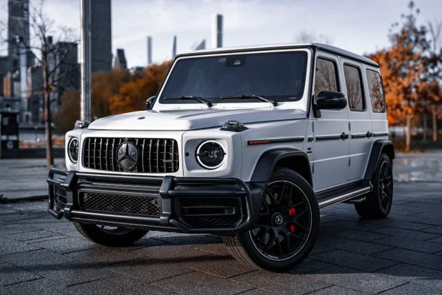 A white Mercedes-Benz G-Class SUV parked on a street during autumn.