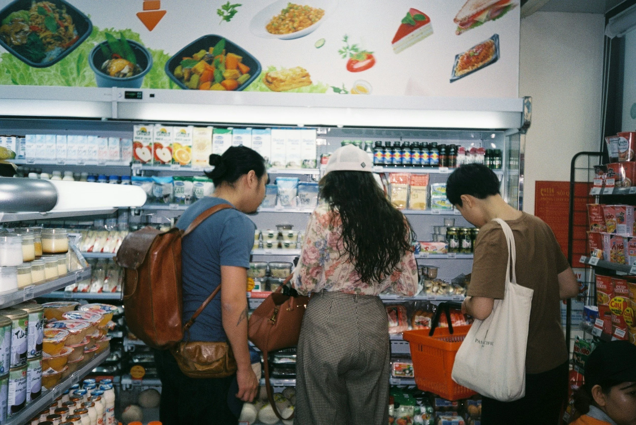 Three people shopping in a grocery store aisle with dairy and beverage products.