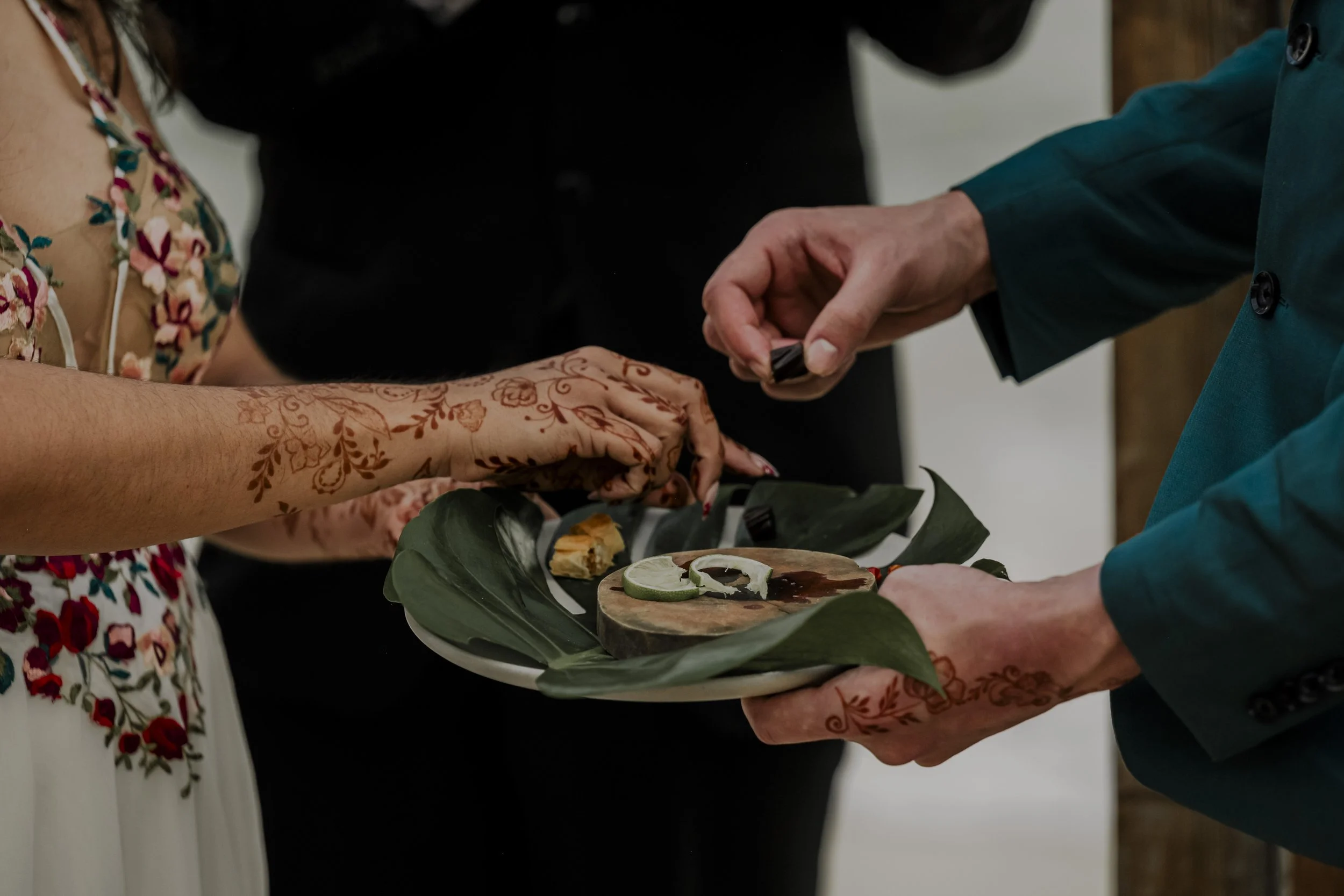 Person with henna tattoos on arm receiving a piece of cake at a celebration, with another person holding a plate of desserts.