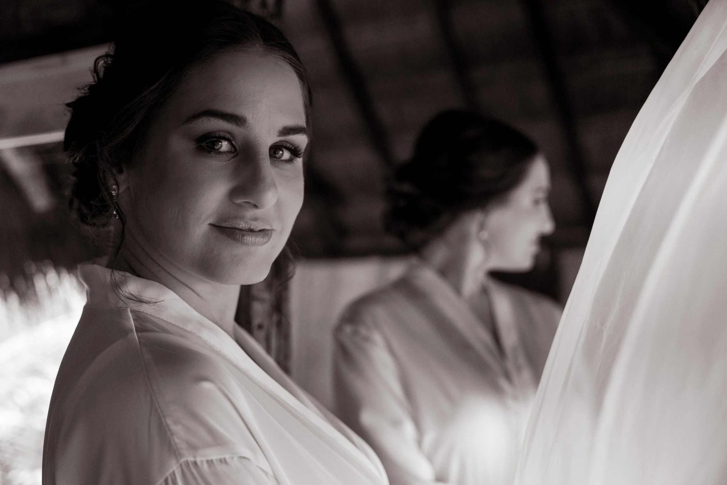 Black and white photo of two women in robes, one in the foreground looking at the camera with a gentle smile, and the other in the background with focus on her profile.