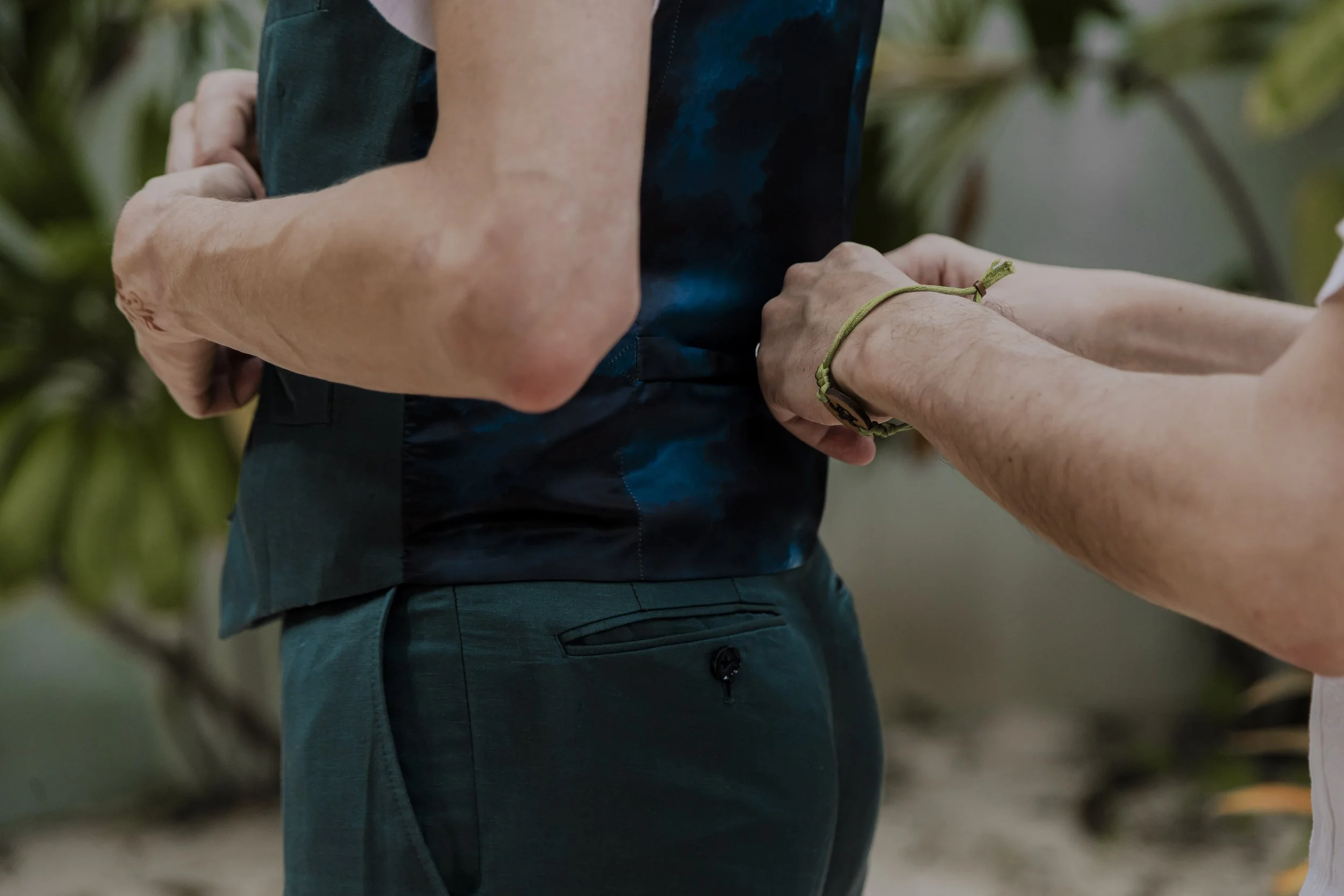 Person in blue attire holding hands with another person, one hand with a watch, in an outdoor setting.