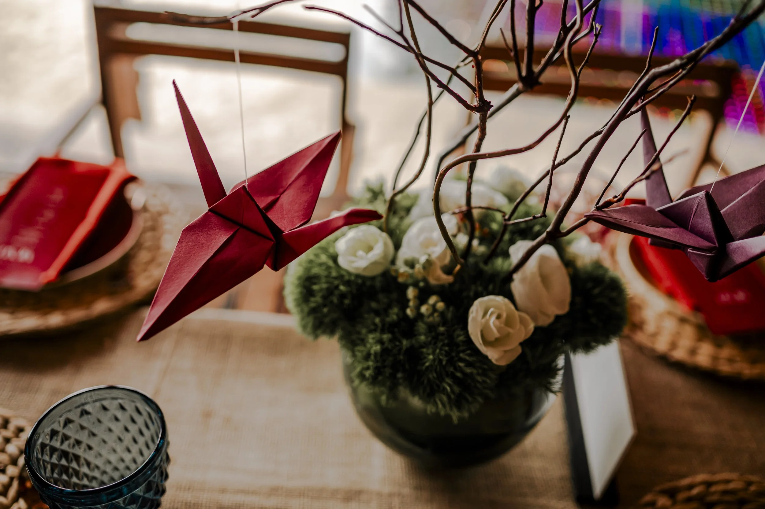 Decorative origami paper cranes hanging over a flower arrangement with white roses and green foliage.