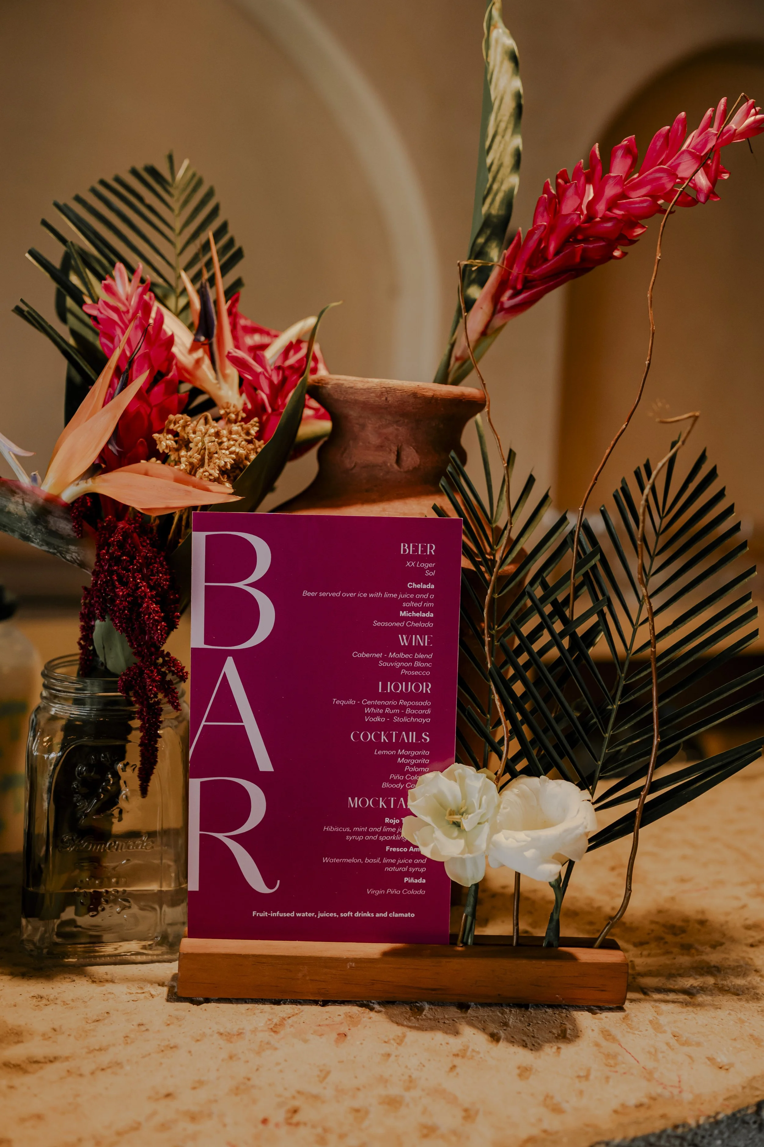 A decorative arrangement with tropical flowers, green leaves, and a menu on a stand, placed on a marble counter.