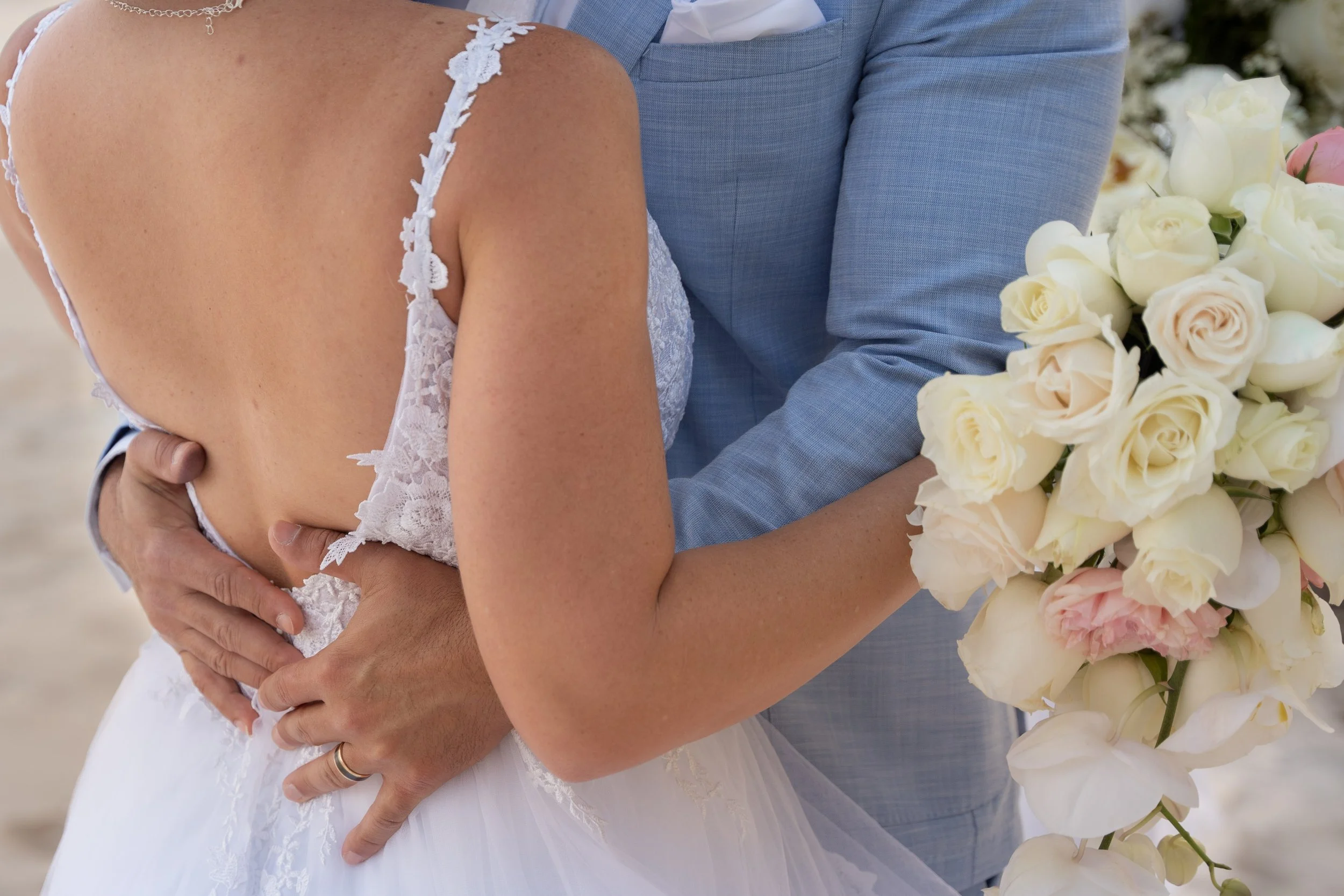 Close-up of a bride and groom holding each other, with the bride holding a bouquet of white and pink roses, during a wedding celebration.