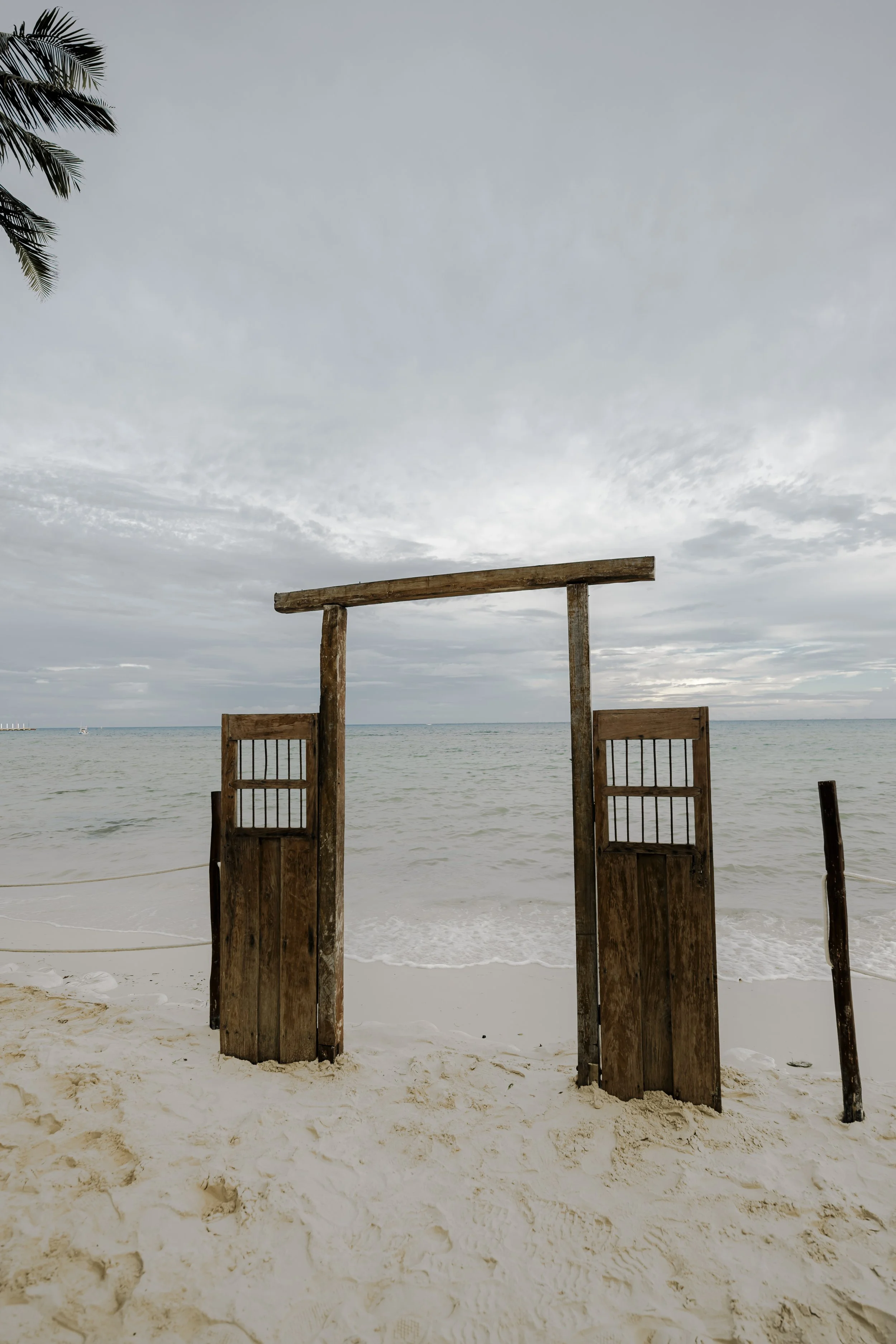 Wooden beach gate on sandy shore with ocean and cloudy sky in background.