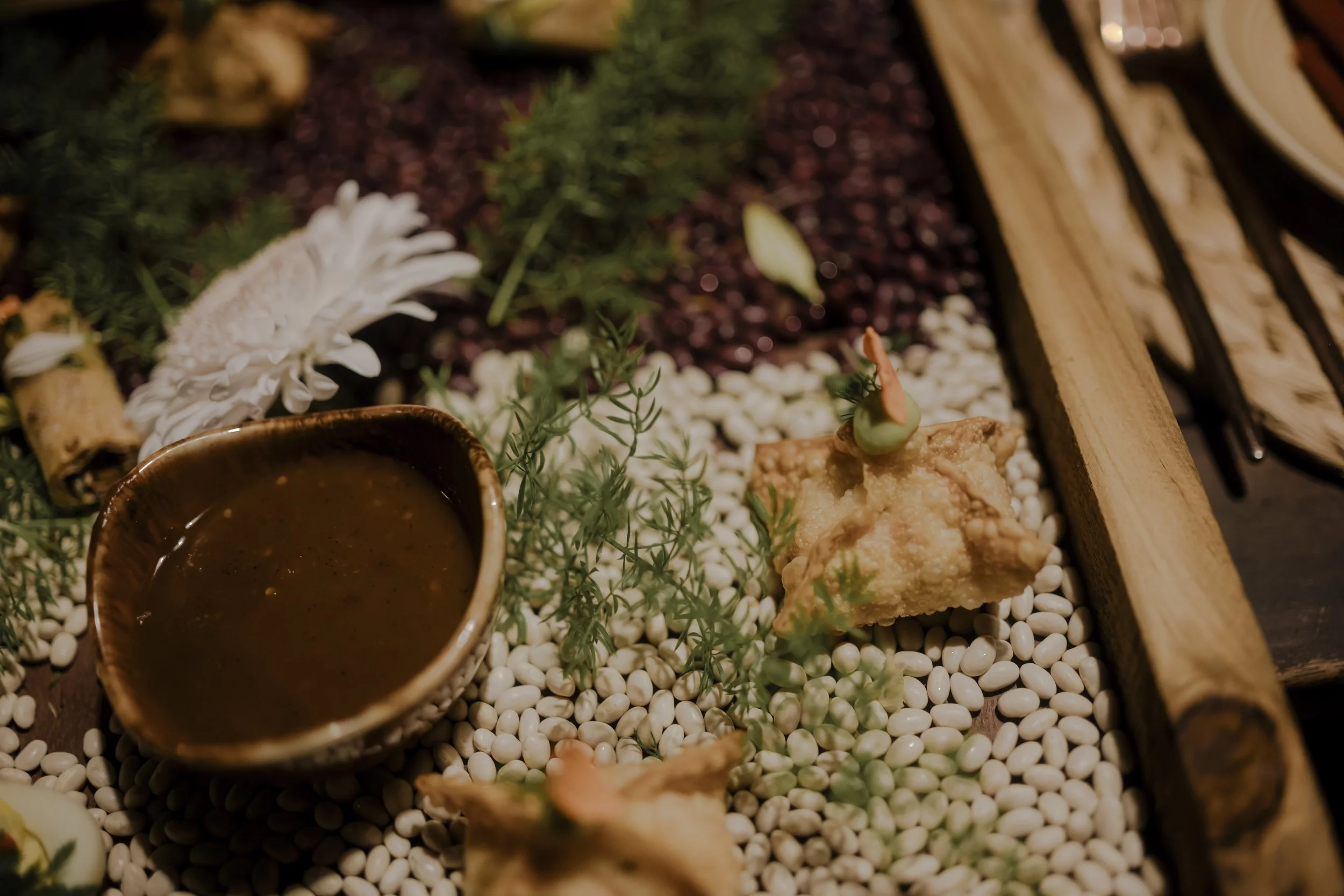 Asian appetizer platter with dipping sauce, fried tofu, vegetables, and flowers on white beans