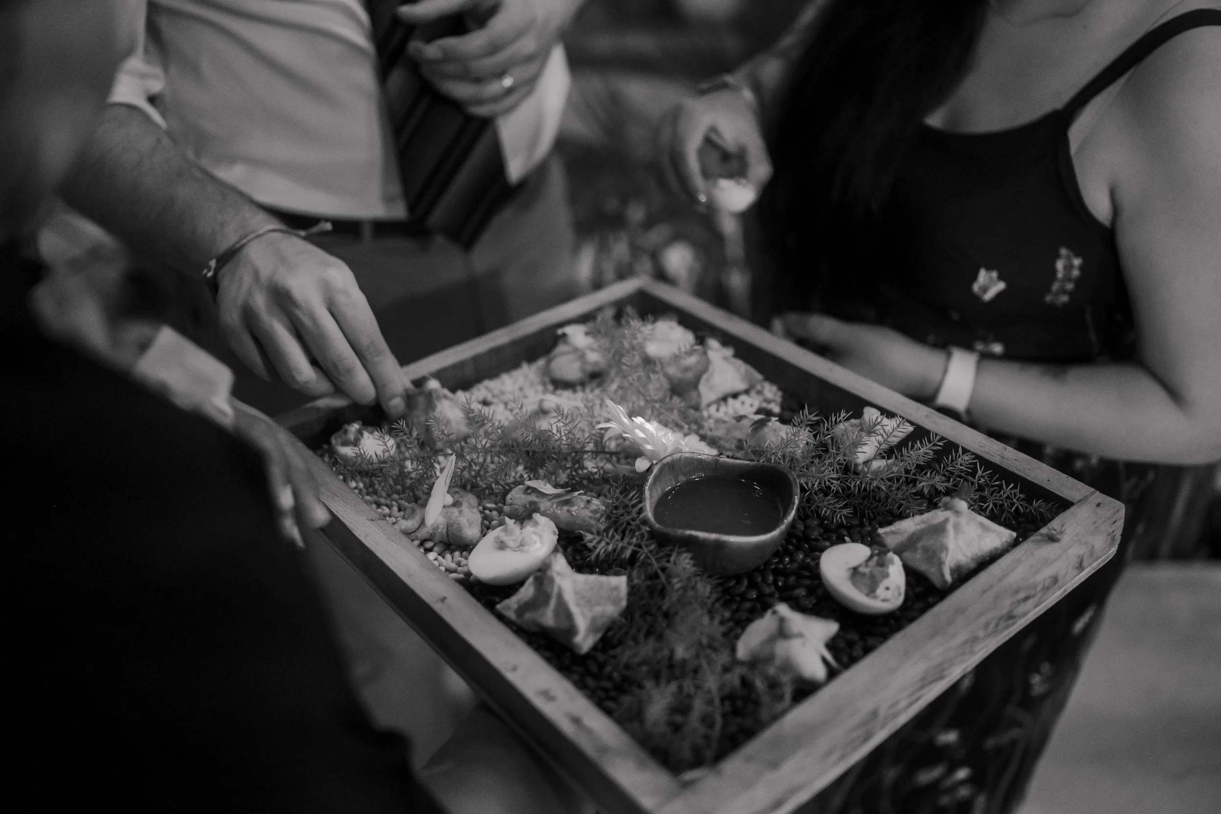 A group of people gathered around a tray with small decorations, greenery, and a small bowl, possibly for a ceremonial or religious purpose.