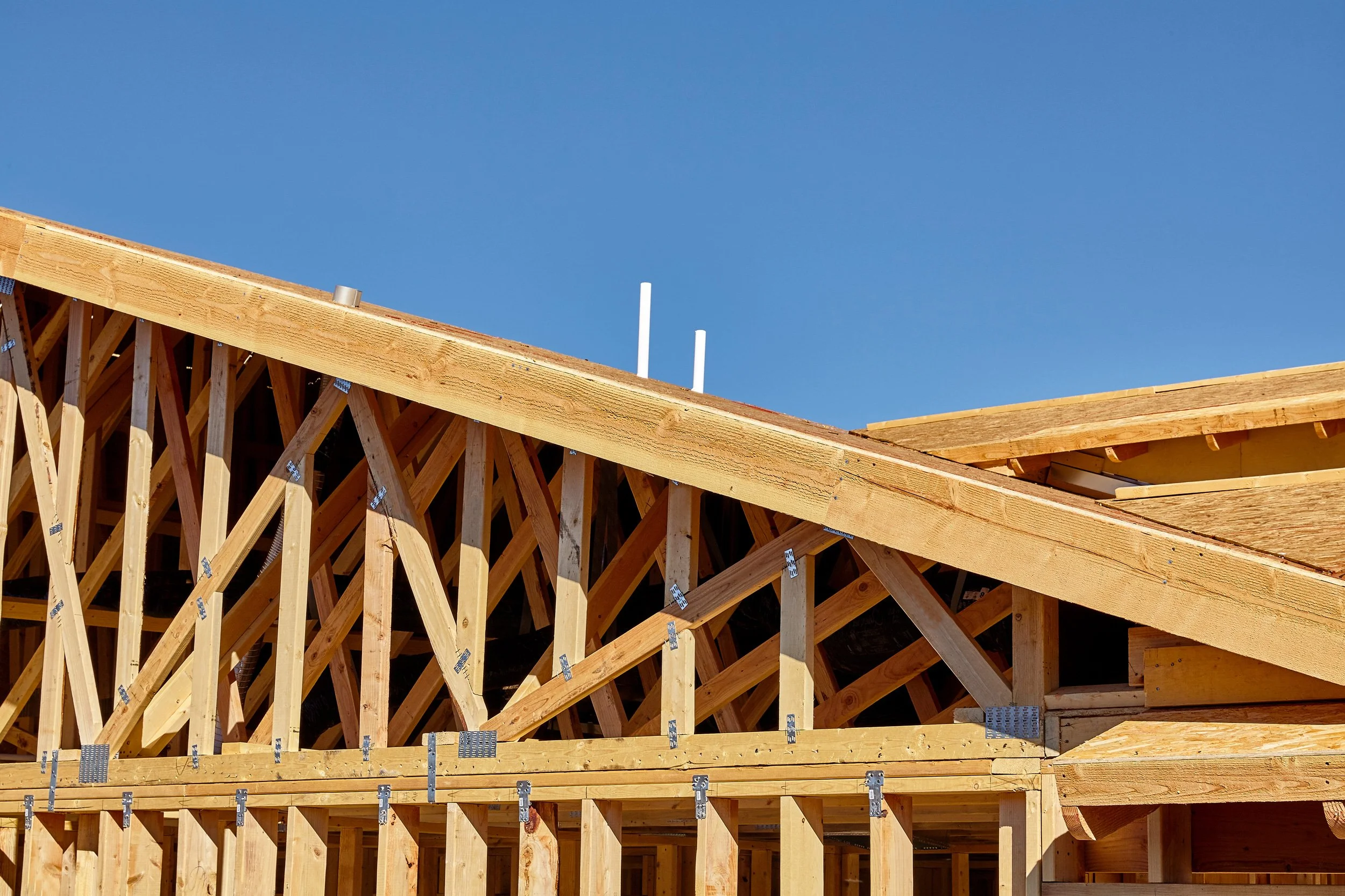 Wooden house framing under construction against a clear blue sky.