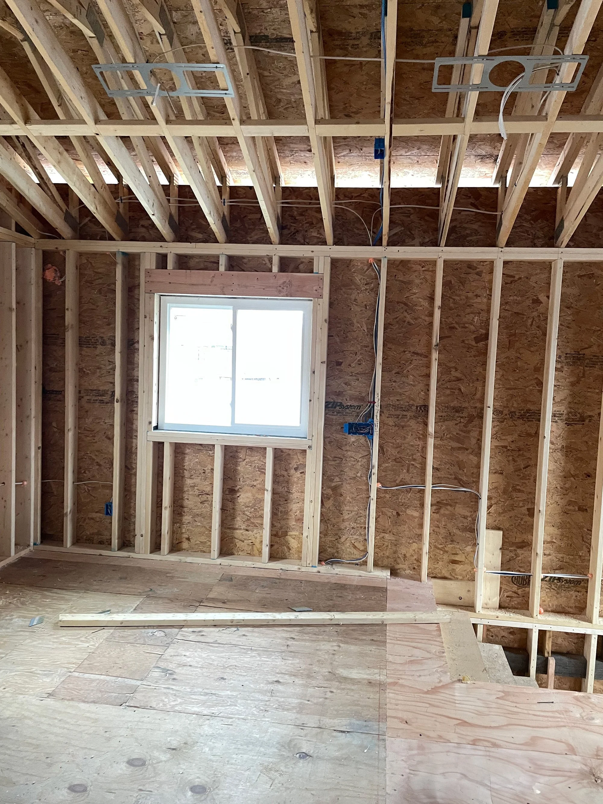 Interior of a house under construction with exposed wooden framing, a window, and electrical wiring.