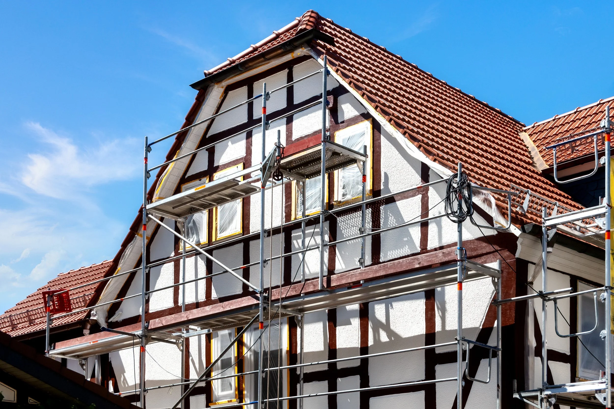 House under renovation with scaffolding around it and a steep red tile roof.