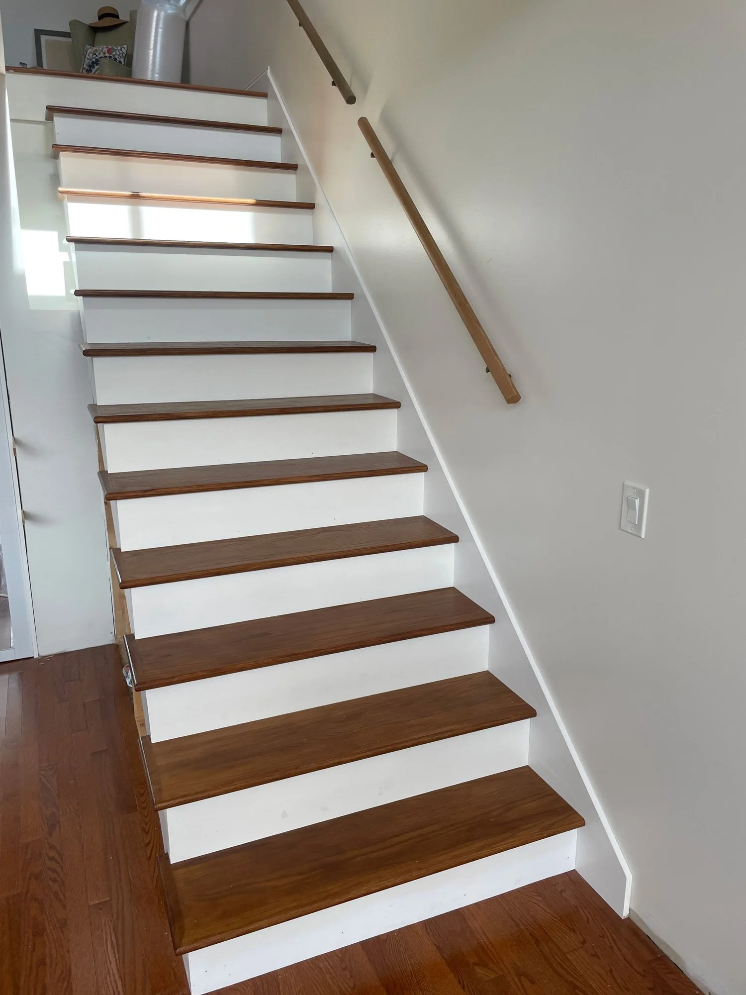Wooden staircase with a single handrail on the right side, leading to an upper level, with white risers and dark wooden treads.