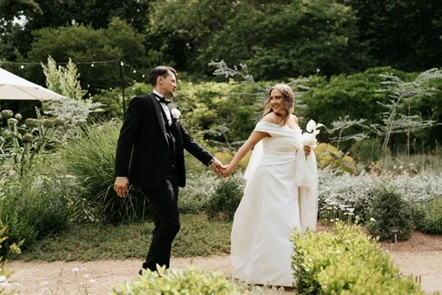 Laurie’s customers, Mariana and Carmen holding hands on a green lawn on their wedding day.