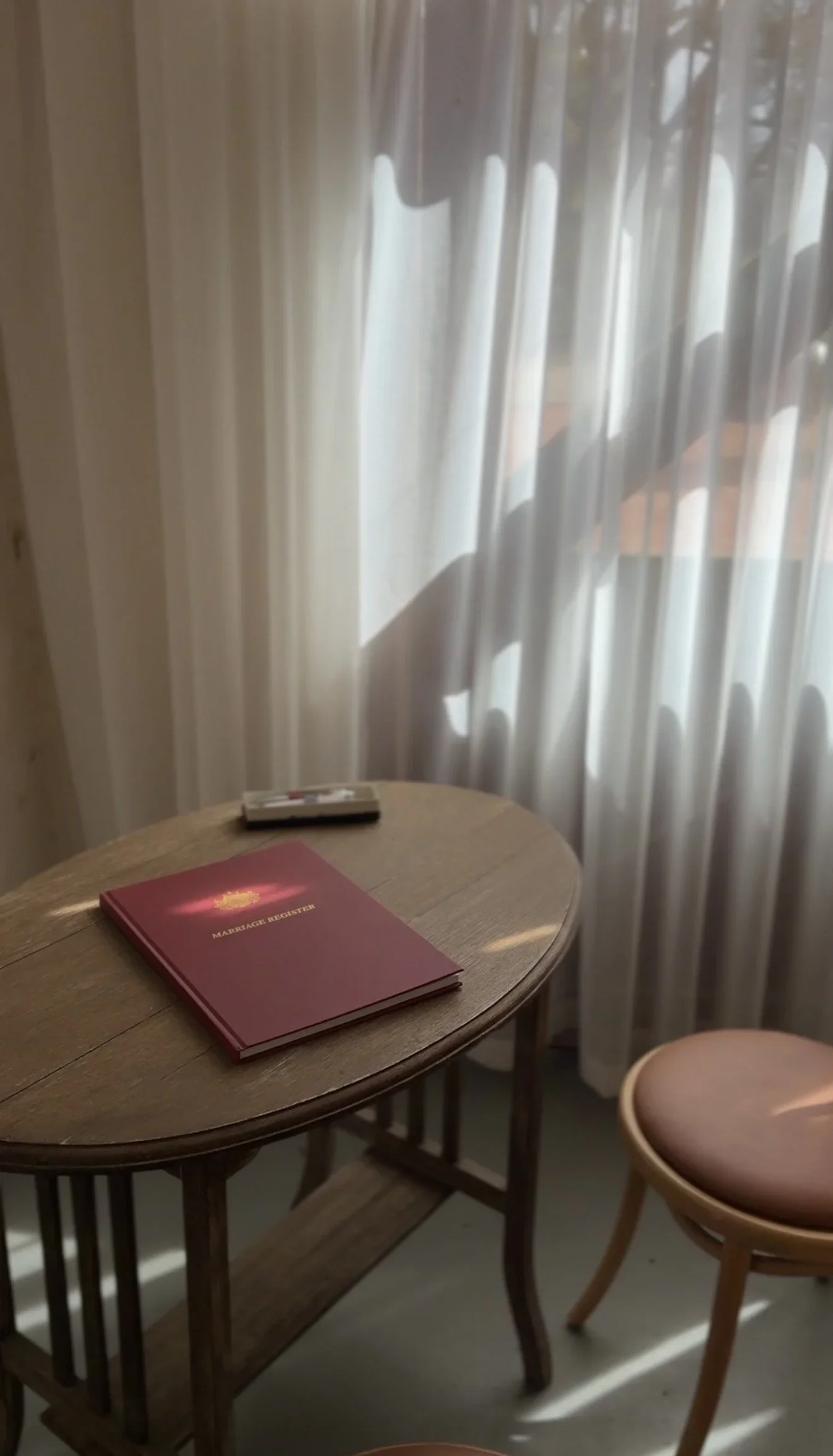 The red marriage register resting on an oak table beside a sheer curtain in soft light