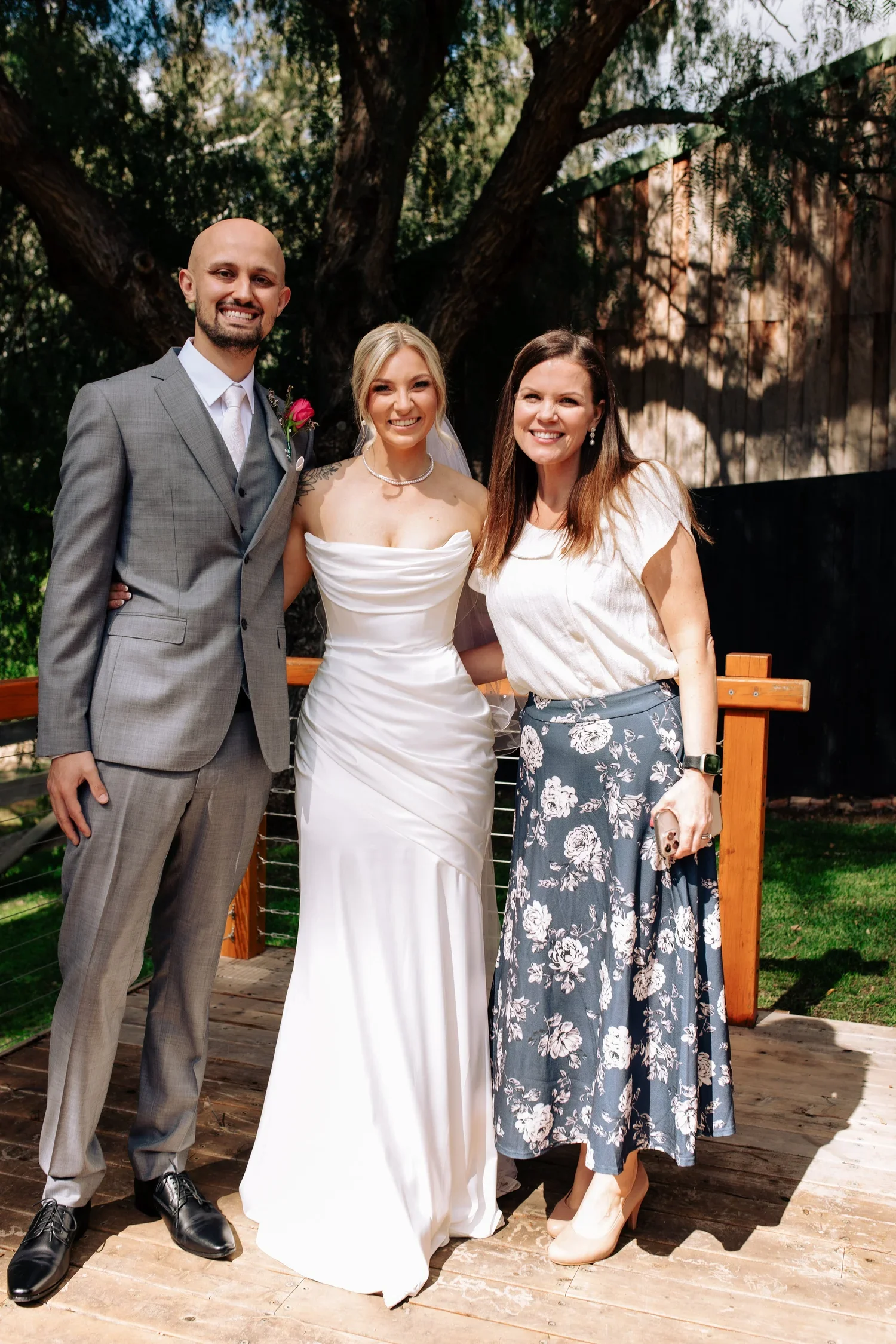Niamh Dillon, Adelaide marriage celebrant, standing with a newly married couple on a timber deck under gum trees