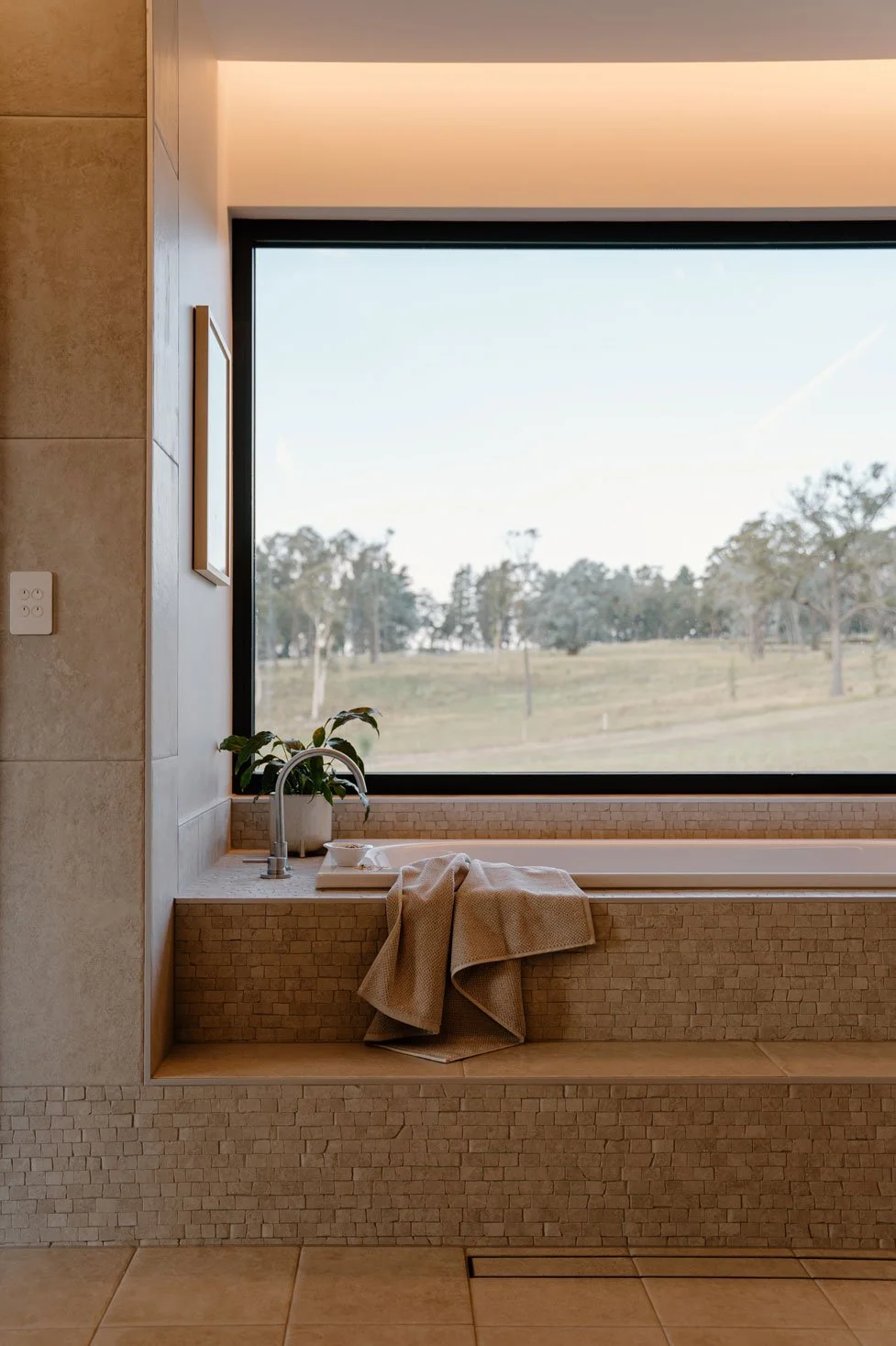 bathtub with a towel hanging over the edge. The window above looks out to an open field with trees in the distance.