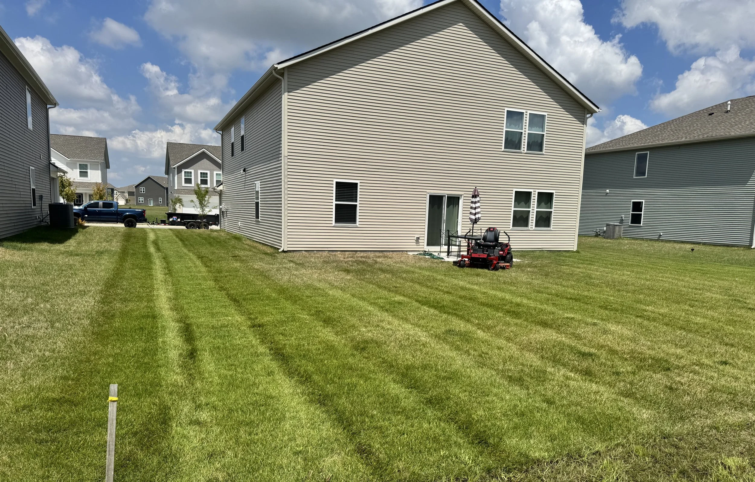 A backyard with freshly mowed grass and houses in the background on a sunny day with a partly cloudy sky.