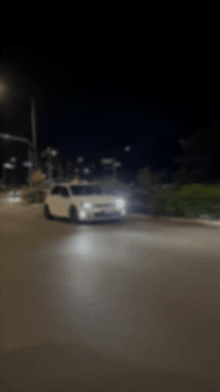 A white car driving on a street at night with streetlights and blurry background.