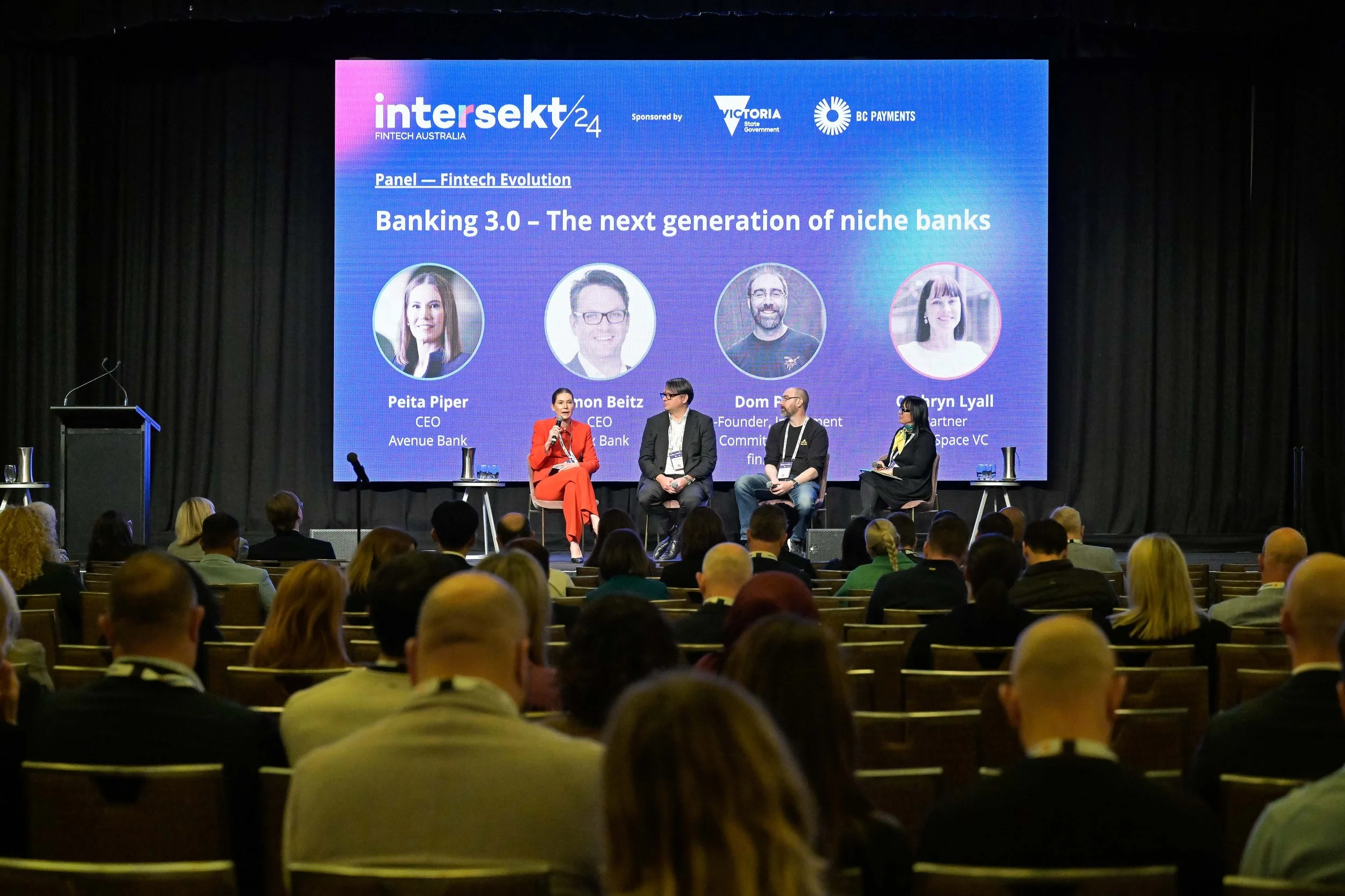 Panel discussion at a conference titled 'Banking 3.0 - The next generation of niche banks,' with four panelists seated on stage and a large screen behind them displaying their photos and names.