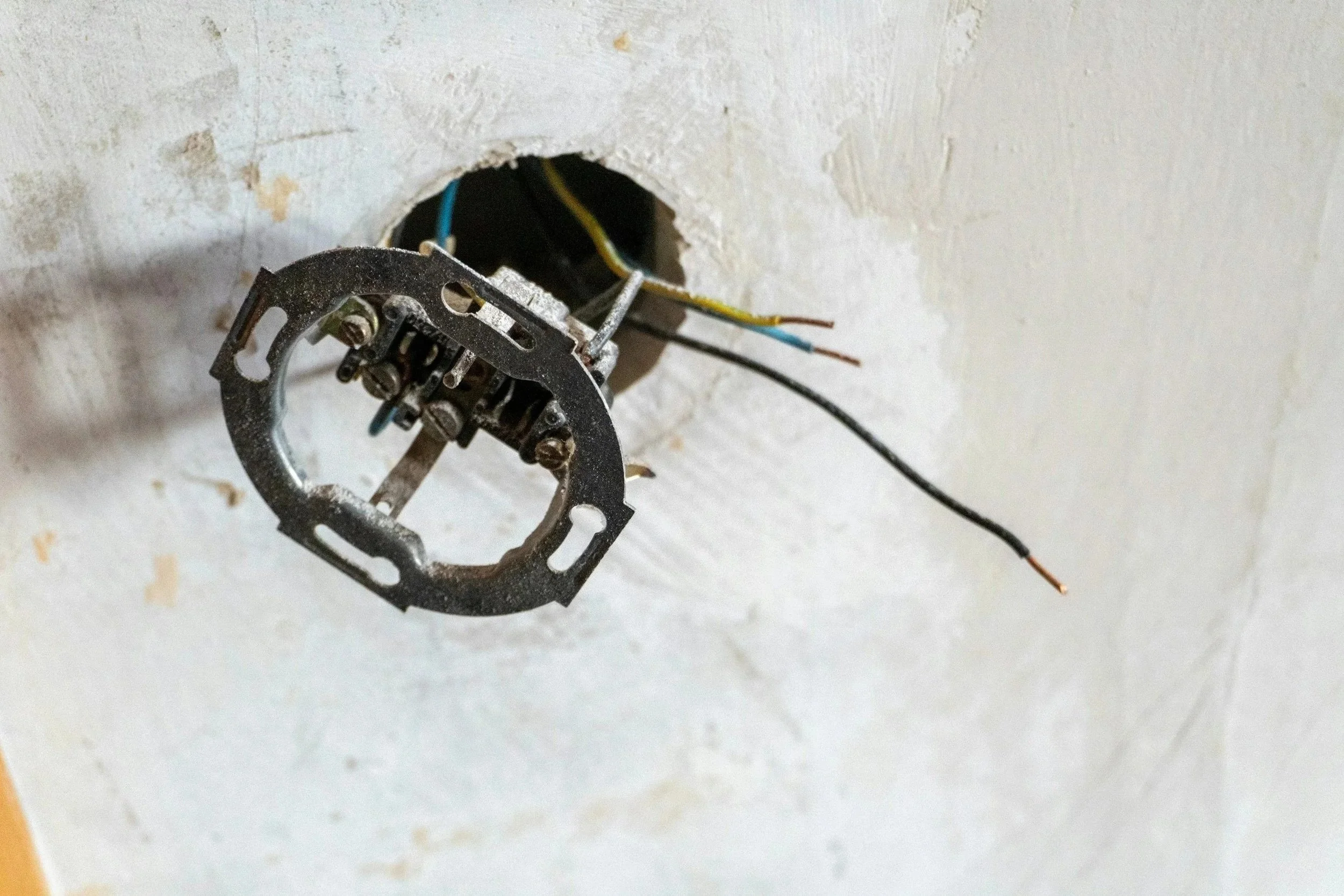An electrical outlet box with four wires protruding from the back, attached to a wall with a rectangular cutout.