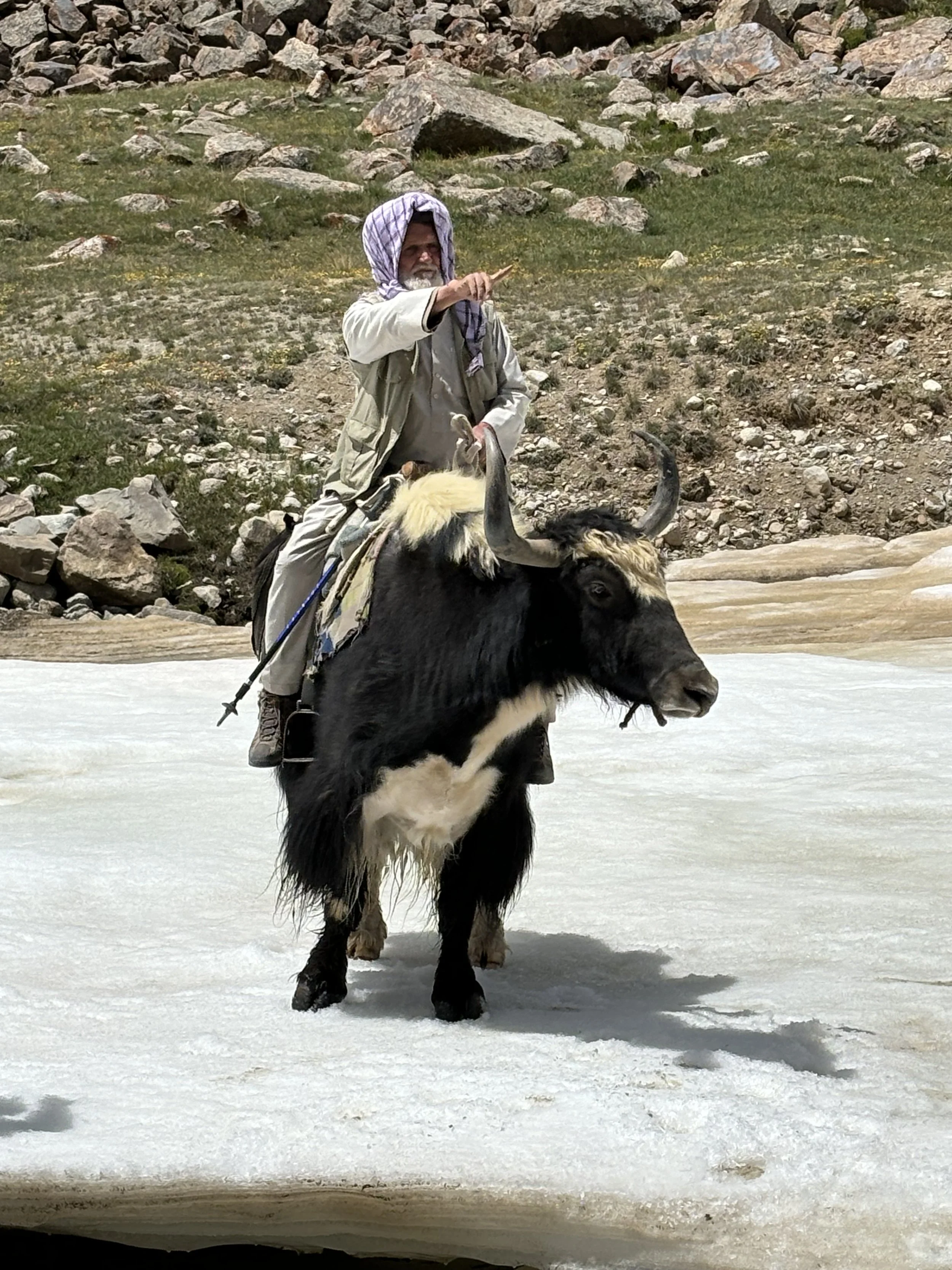 A man riding a yak on a snowy landscape with rocky hills in the background in Afghanistan.