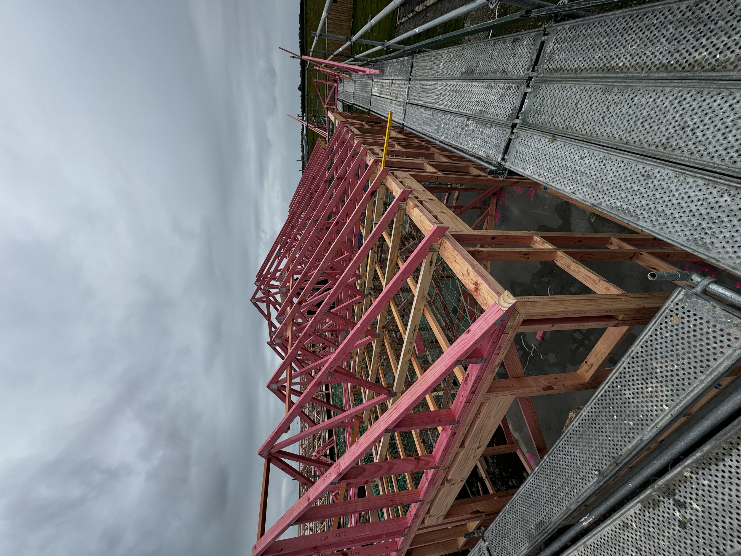 Construction site with wooden scaffolding and metal walkway under a cloudy sky.