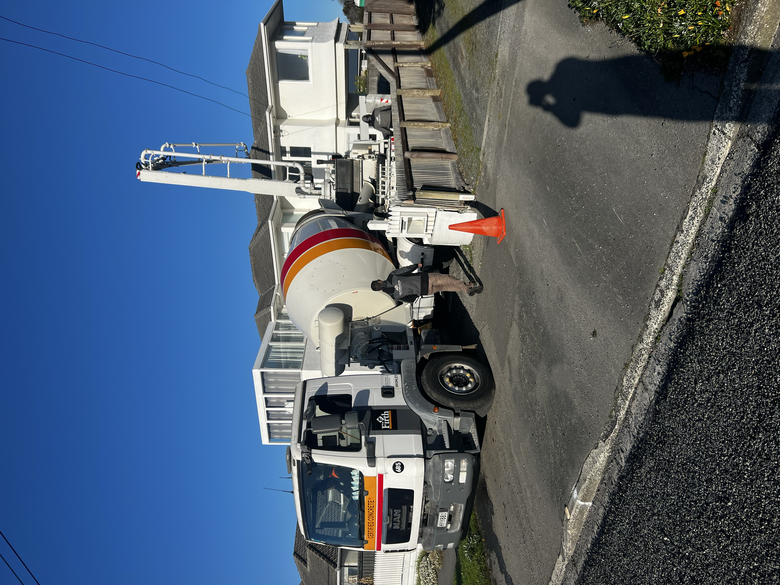 Construction worker standing next to a cement mixer truck on a city street under a clear blue sky.