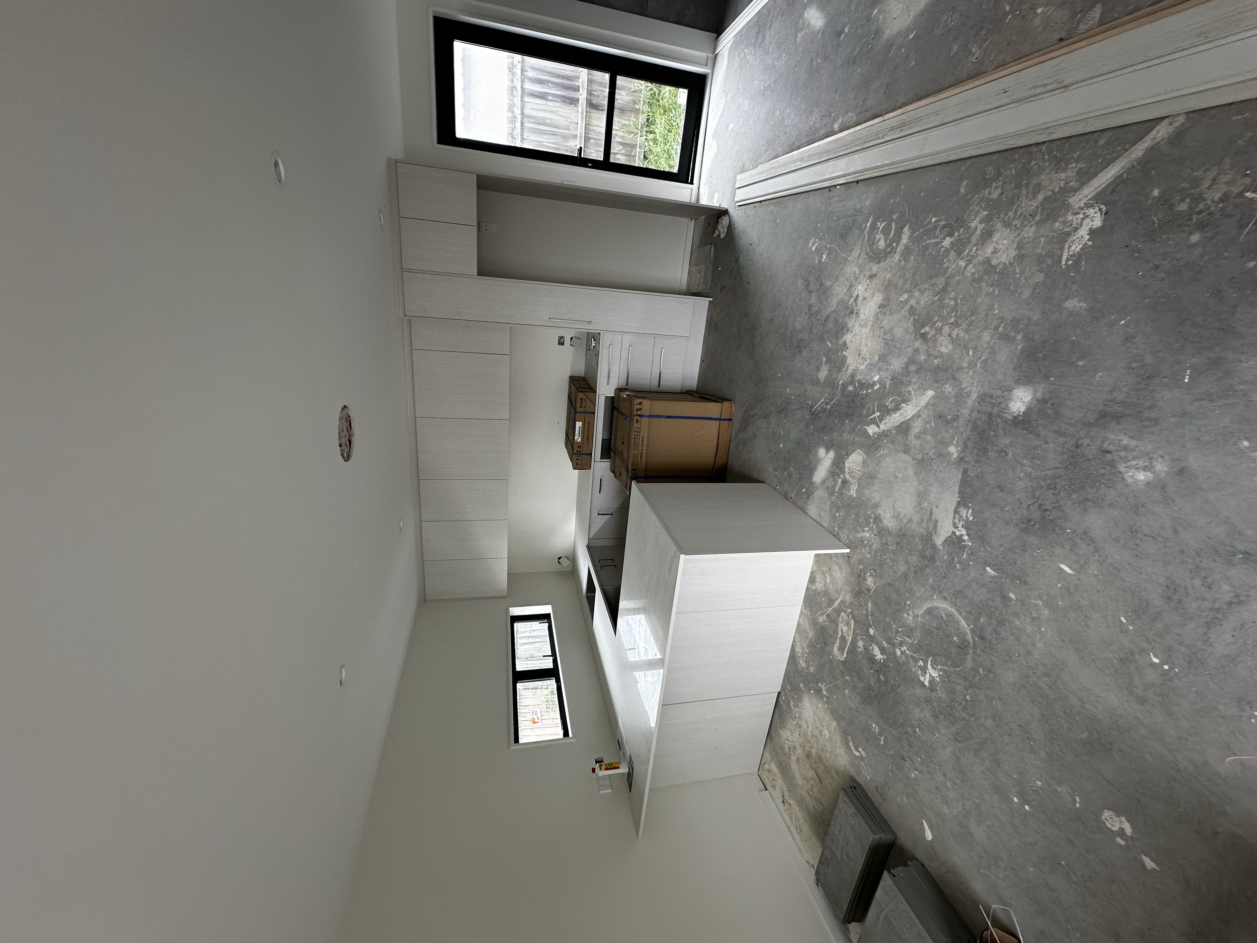 Unfinished kitchen with white cabinetry, a sliding glass door, and construction materials on a concrete floor.
