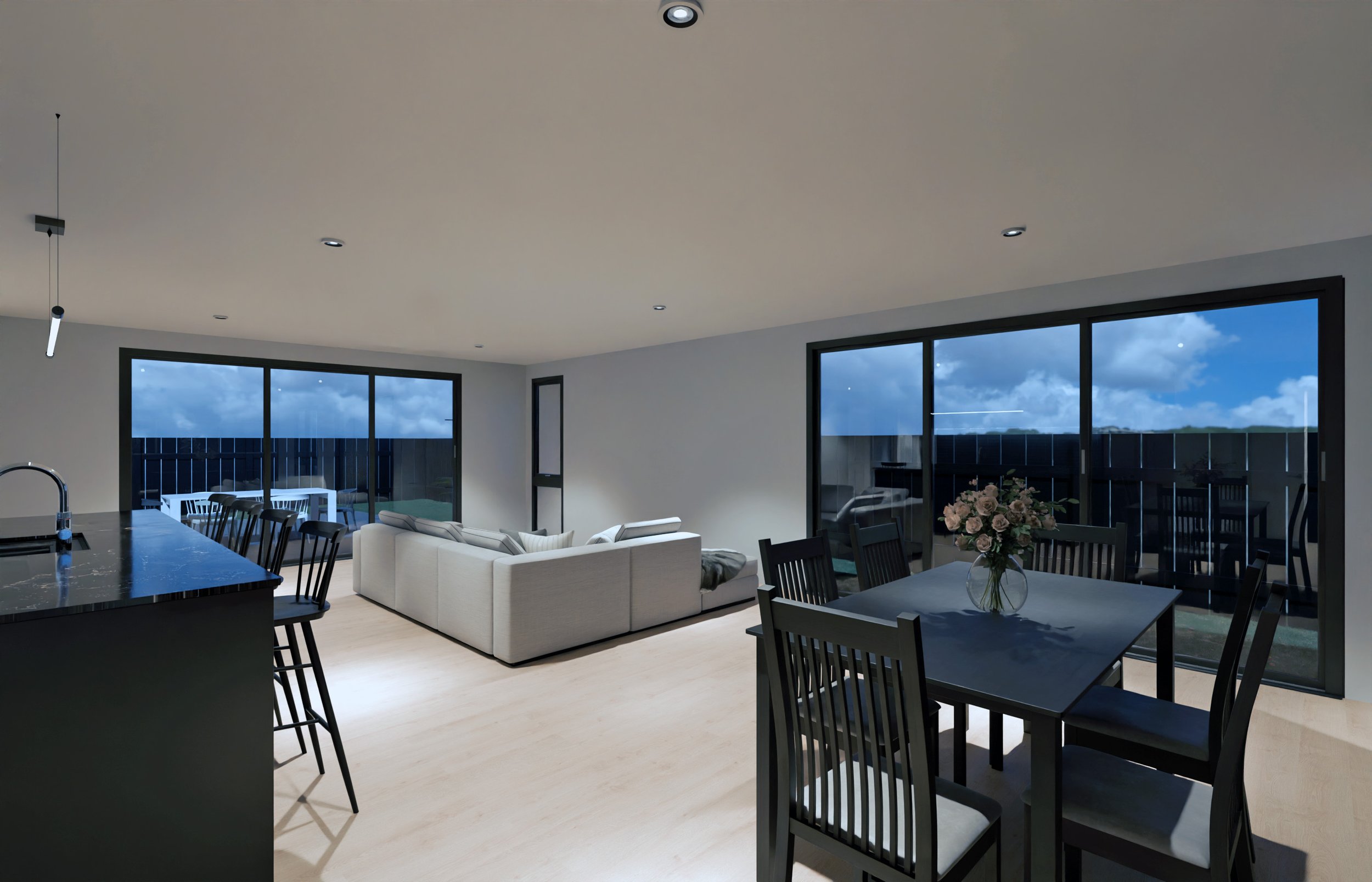 Interior of a modern living and dining area with large glass sliding doors showing an outdoor deck with outdoor furniture and a night sky with clouds.