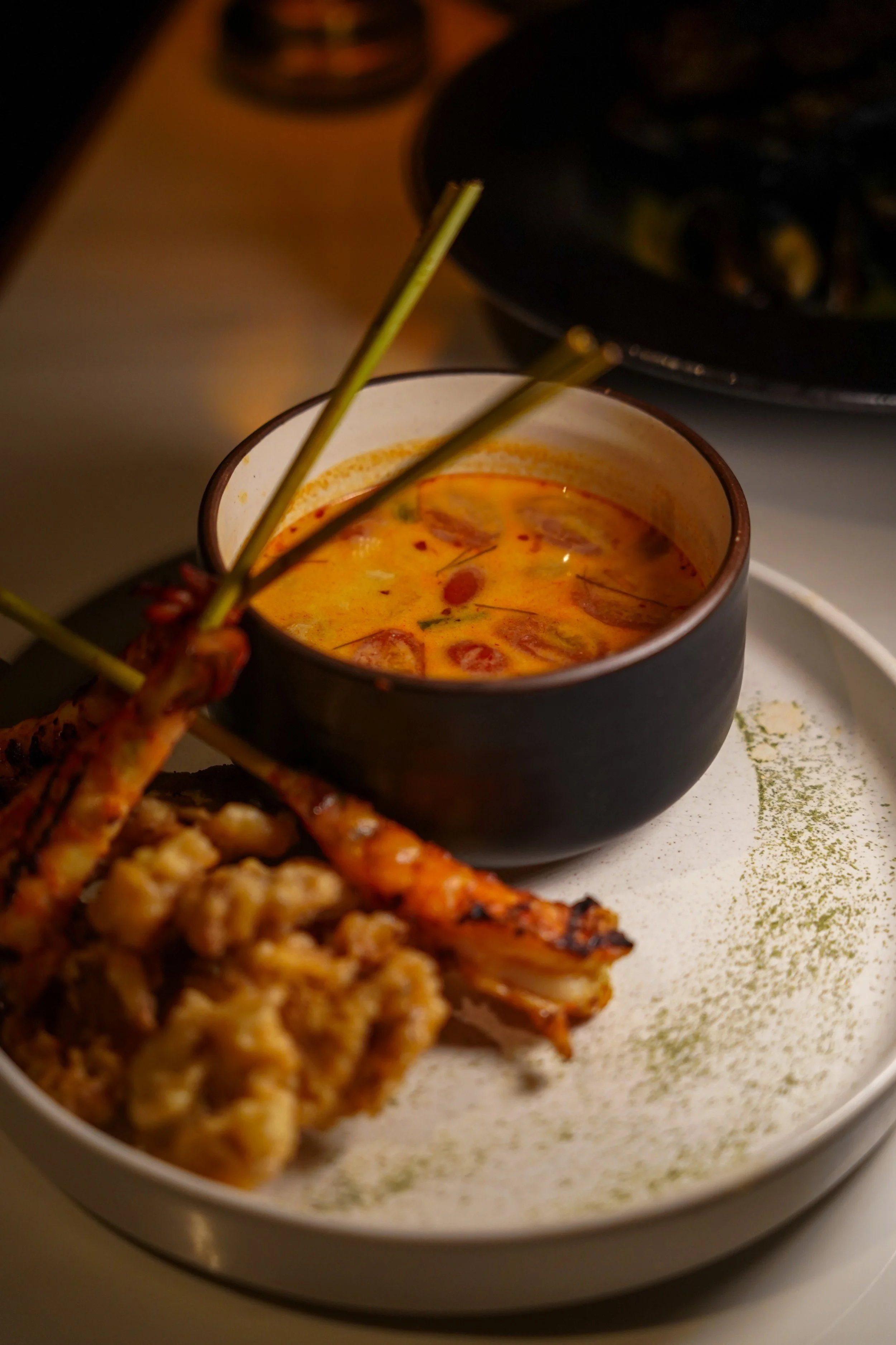 A dish featuring grilled lamb chops with a side of creamy curry sauce garnished with herbs, served on a white plate with a green powder decoration.