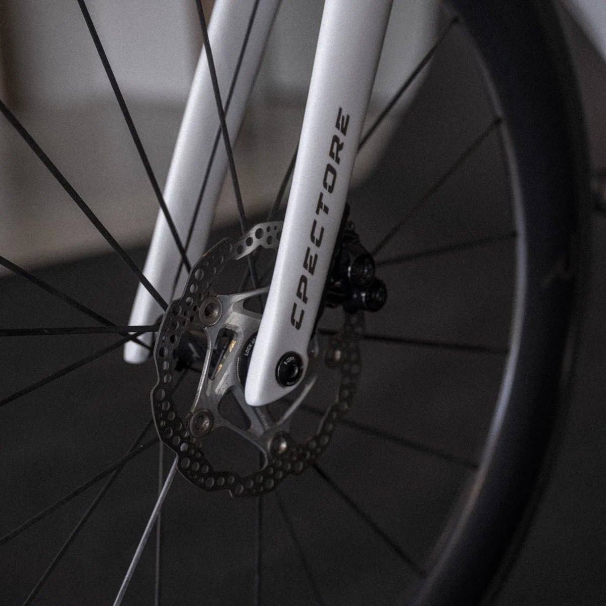 Close-up of a white bicycle front fork with the brand name 'COPPESTORE,' a disc brake rotor, spokes, and part of the tire visible.