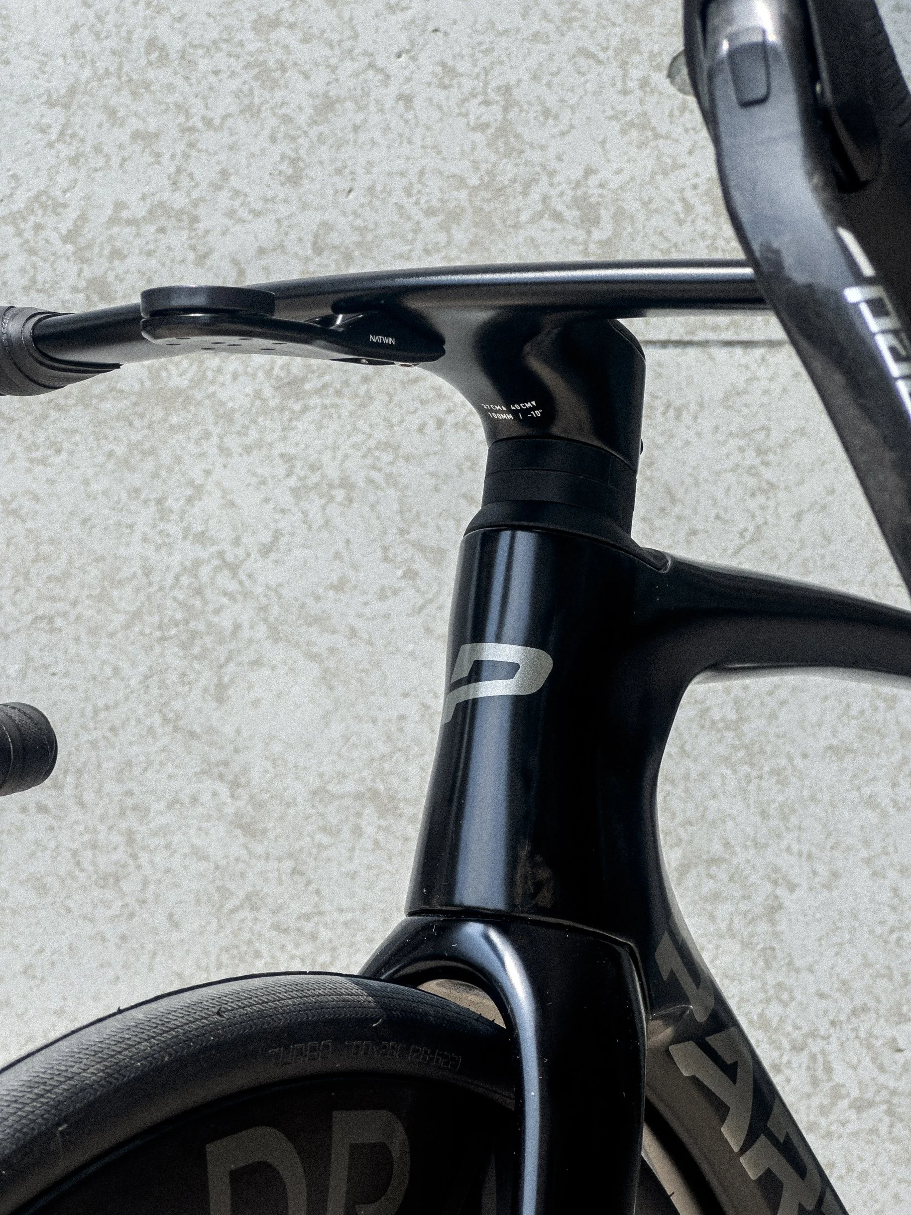 Close-up view of the front part of a PARENTESI  black bicycle, focusing on the handlebar and the LOGO with a partial view of the front wheel.