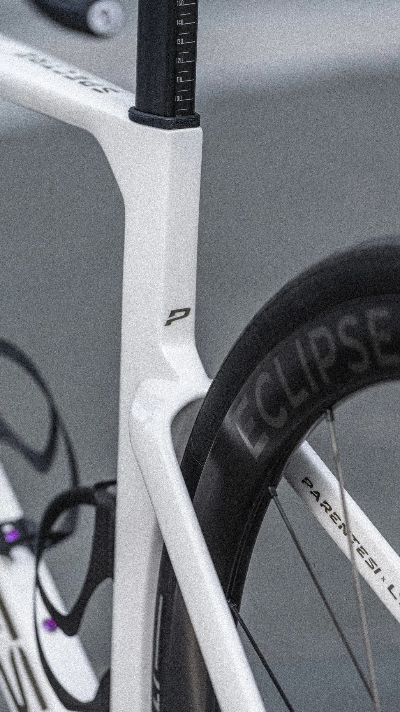 Close-up of a white modern PARENTESI  racing bike with carbon fibre components and black tire labeled "ECLIPSE" and "RAYDN".