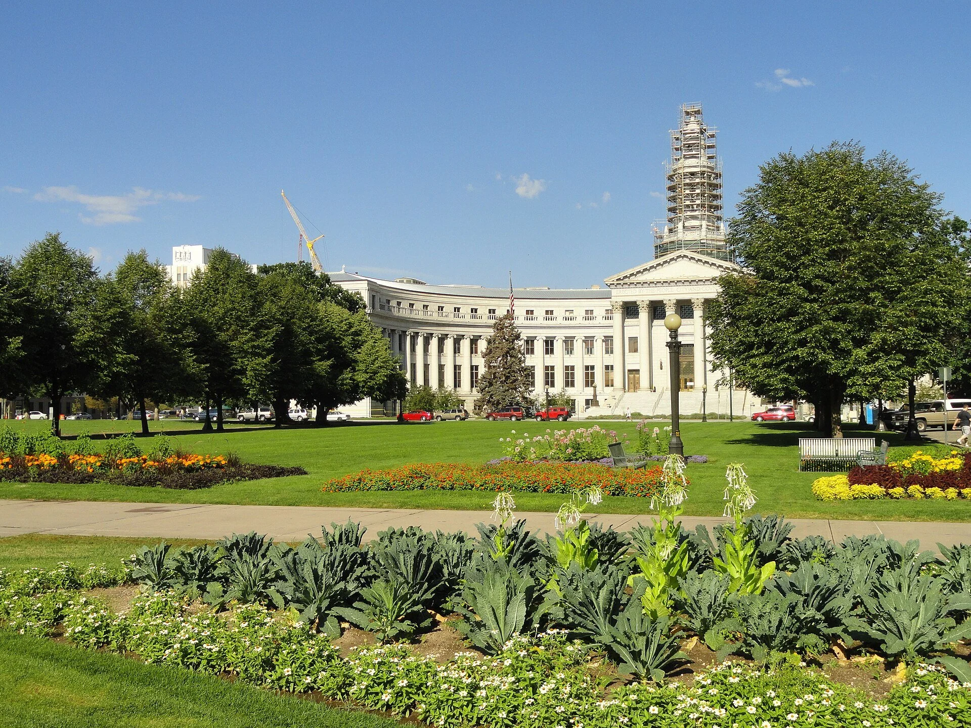 The Denver City and County Building, a curved neoclassical building with a clock tower, seen across the gardens of Civic Center Park.