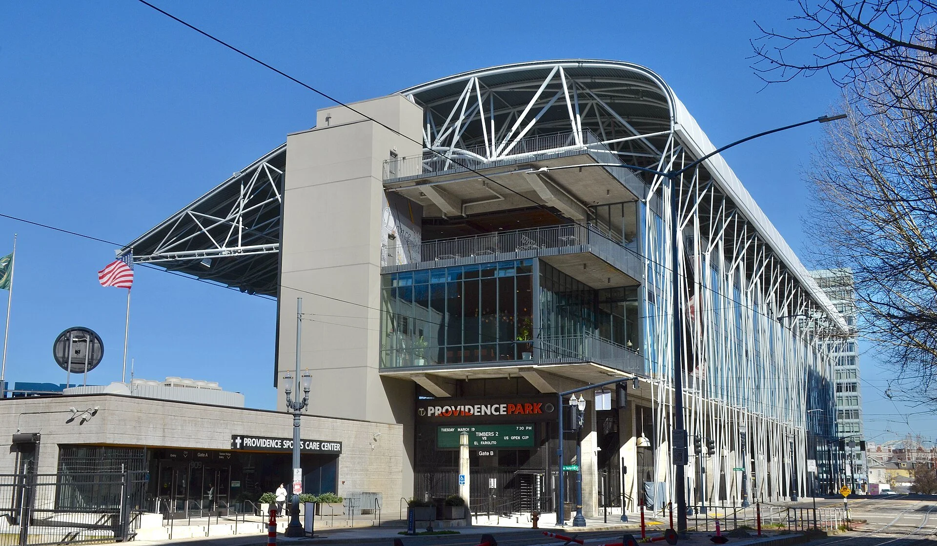 The exterior of Providence Park in Portland, a stadium with a curved metal roof structure and a glass entrance.