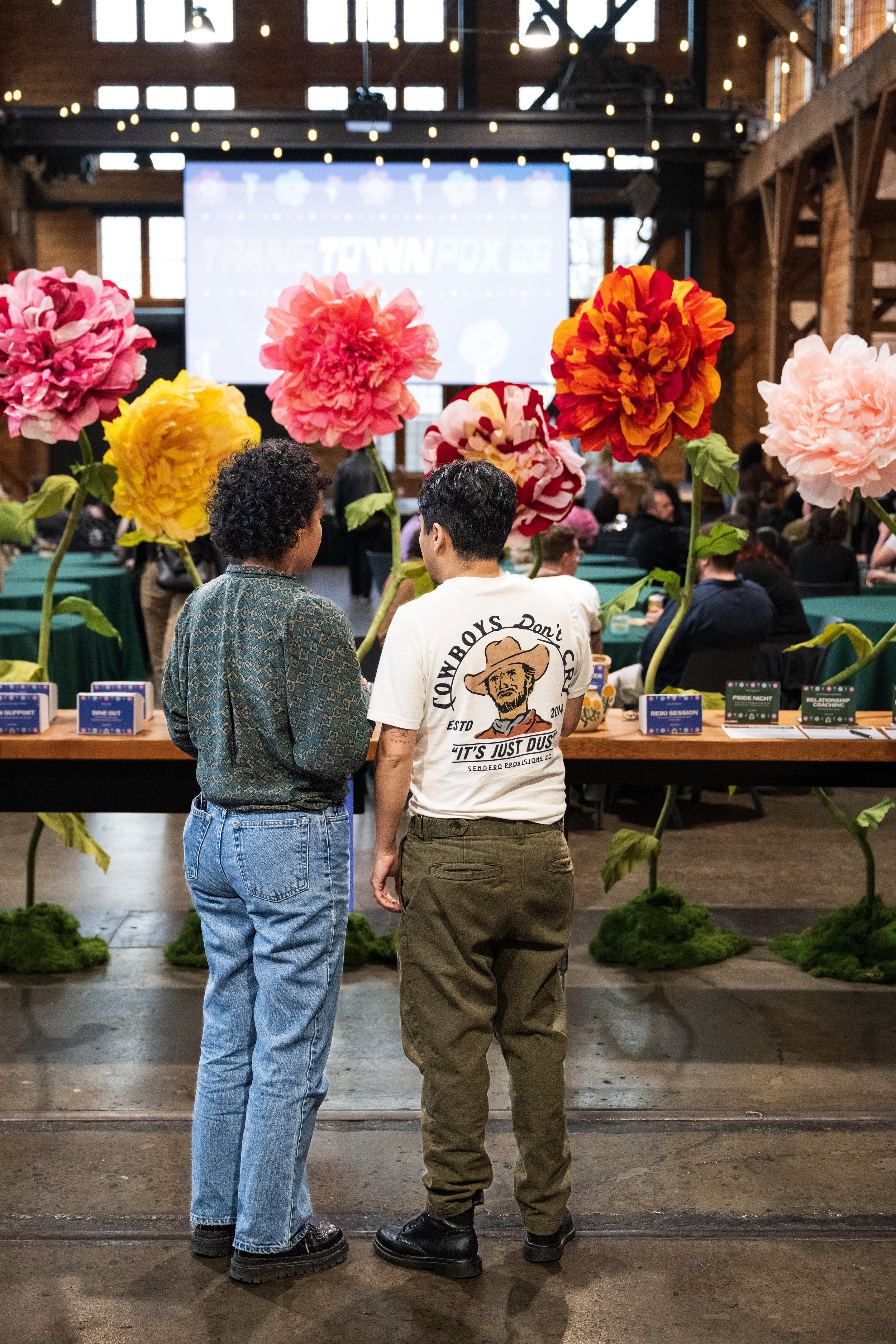 2 brown trans people stand infront of beautiful flowers