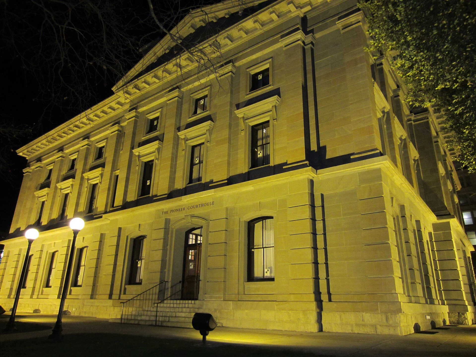 The Pioneer Courthouse in downtown Portland at night, a stone building lit in warm yellow light.