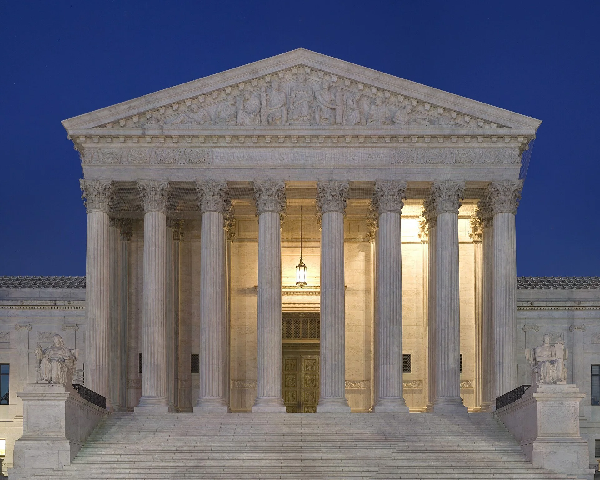 The front of the U.S. Supreme Court building at dusk, its marble columns lit from within under a deep blue sky.