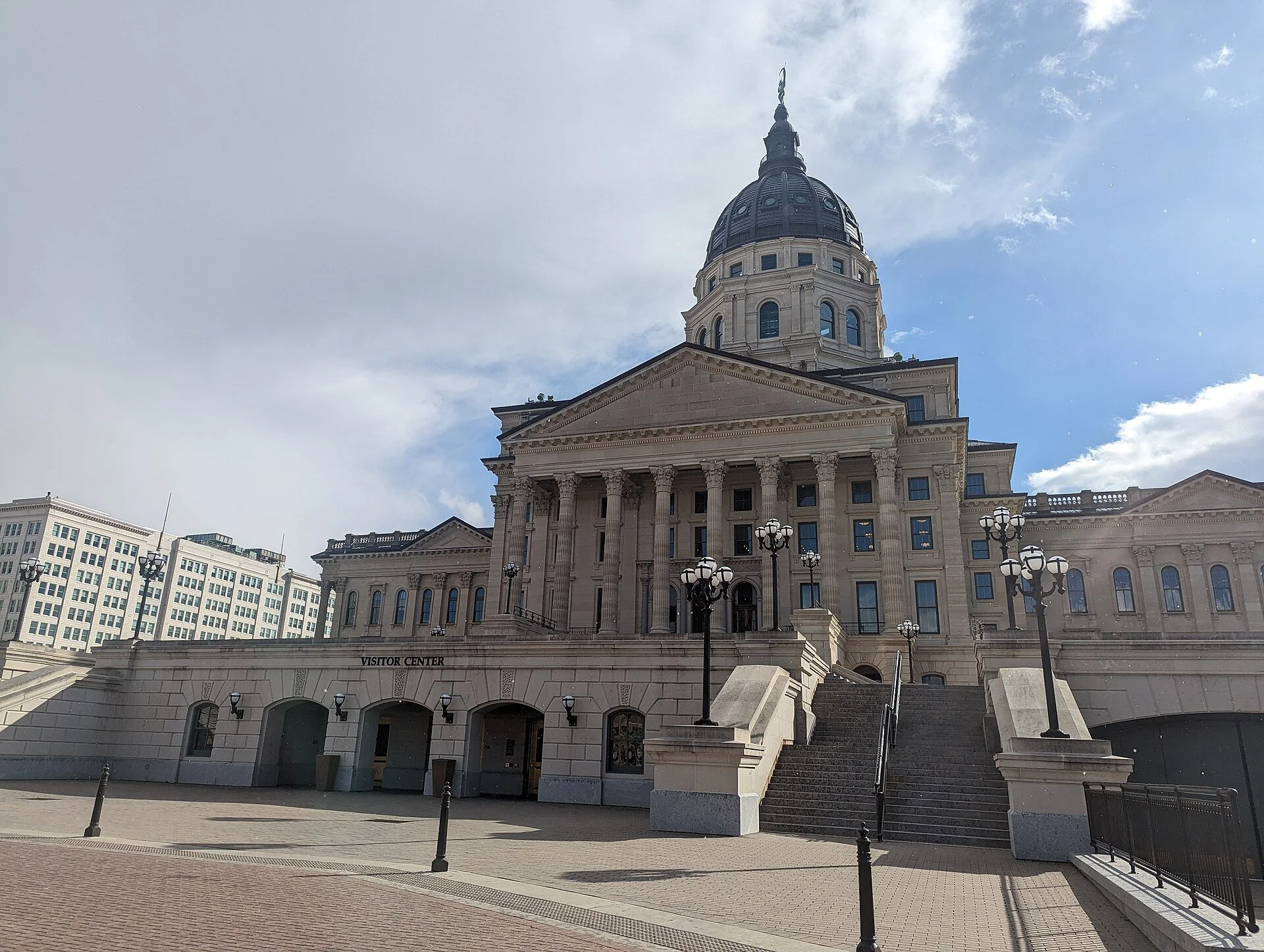 The Kansas State Capitol in Topeka, a domed limestone building with columns and wide front steps, under a pale sky.