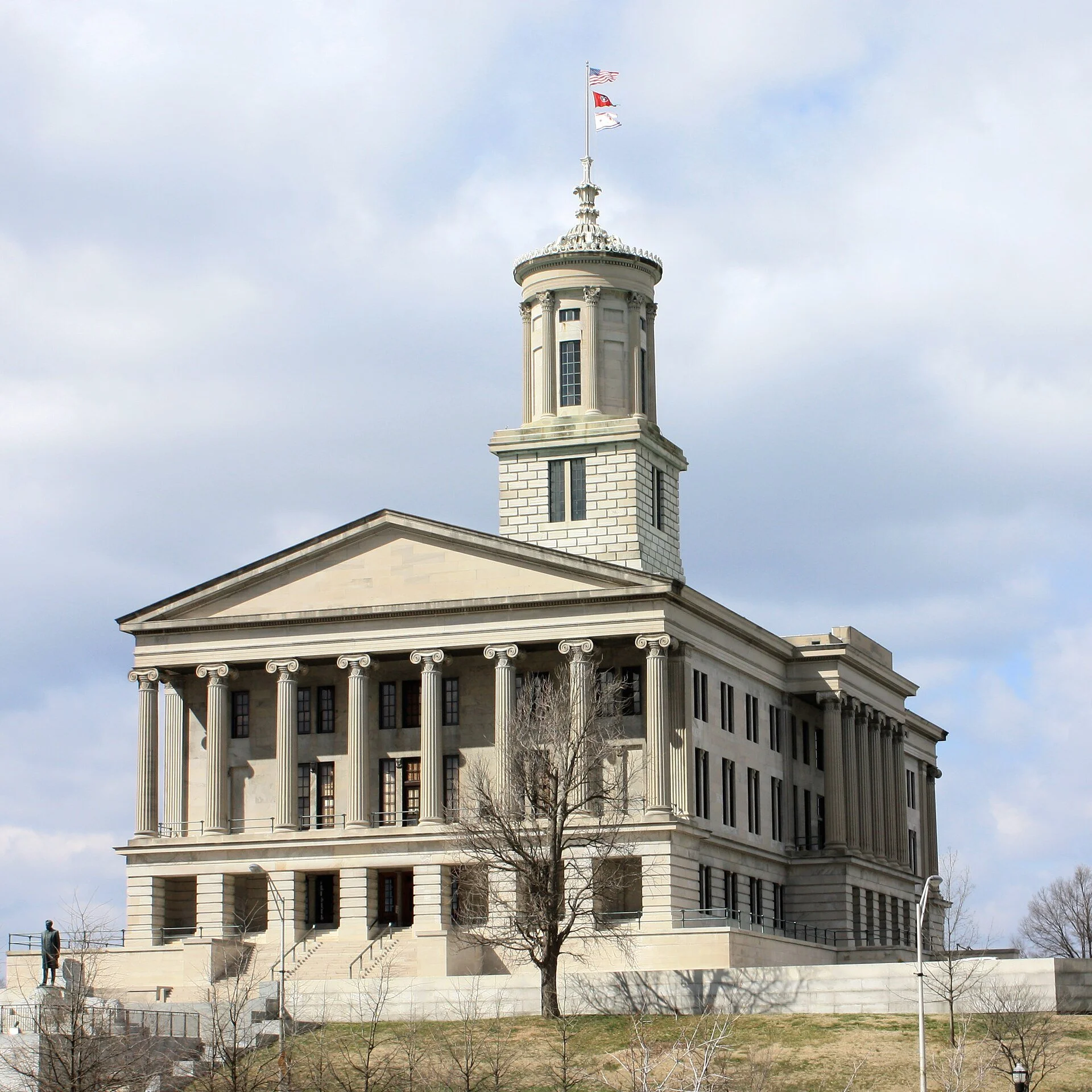 The Tennessee State Capitol in Nashville, a stone building with a tall tower and columned porticos, seen under a cloudy sky.