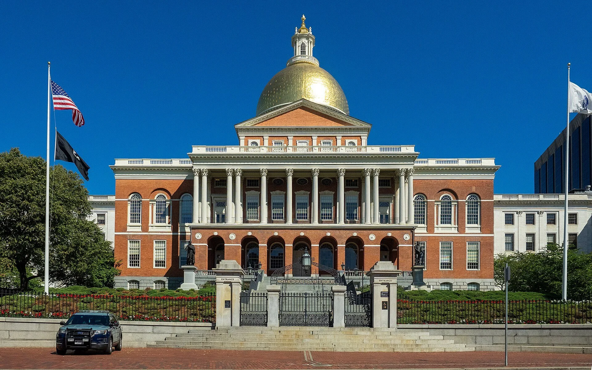 The Massachusetts State House in Boston, a red brick building with white columns and a gold dome, with flags out front.