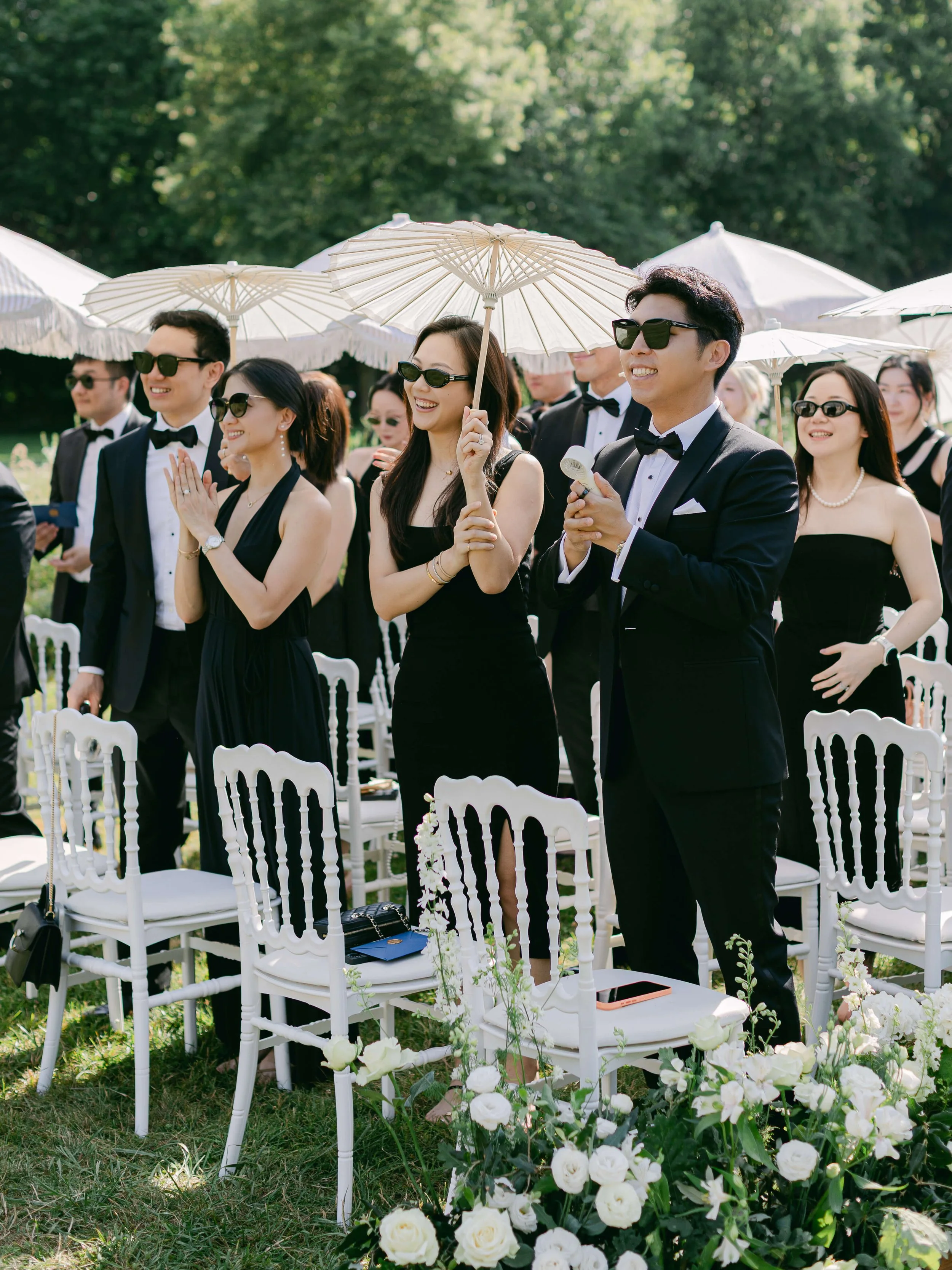 Wedding guests holding parasols during the summer garden ceremony