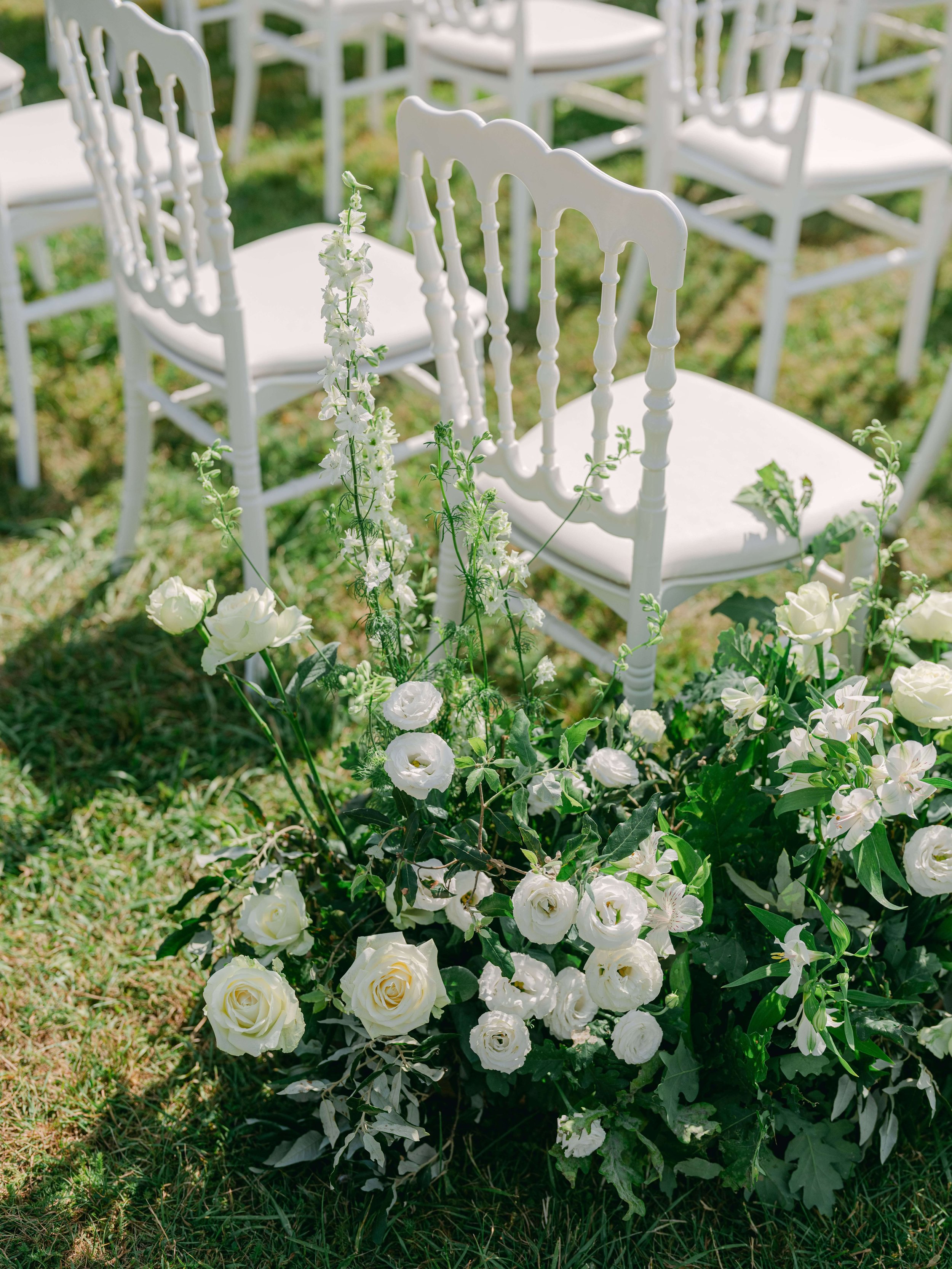 White roses and seasonal flowers arranged along the outdoor ceremony aisle