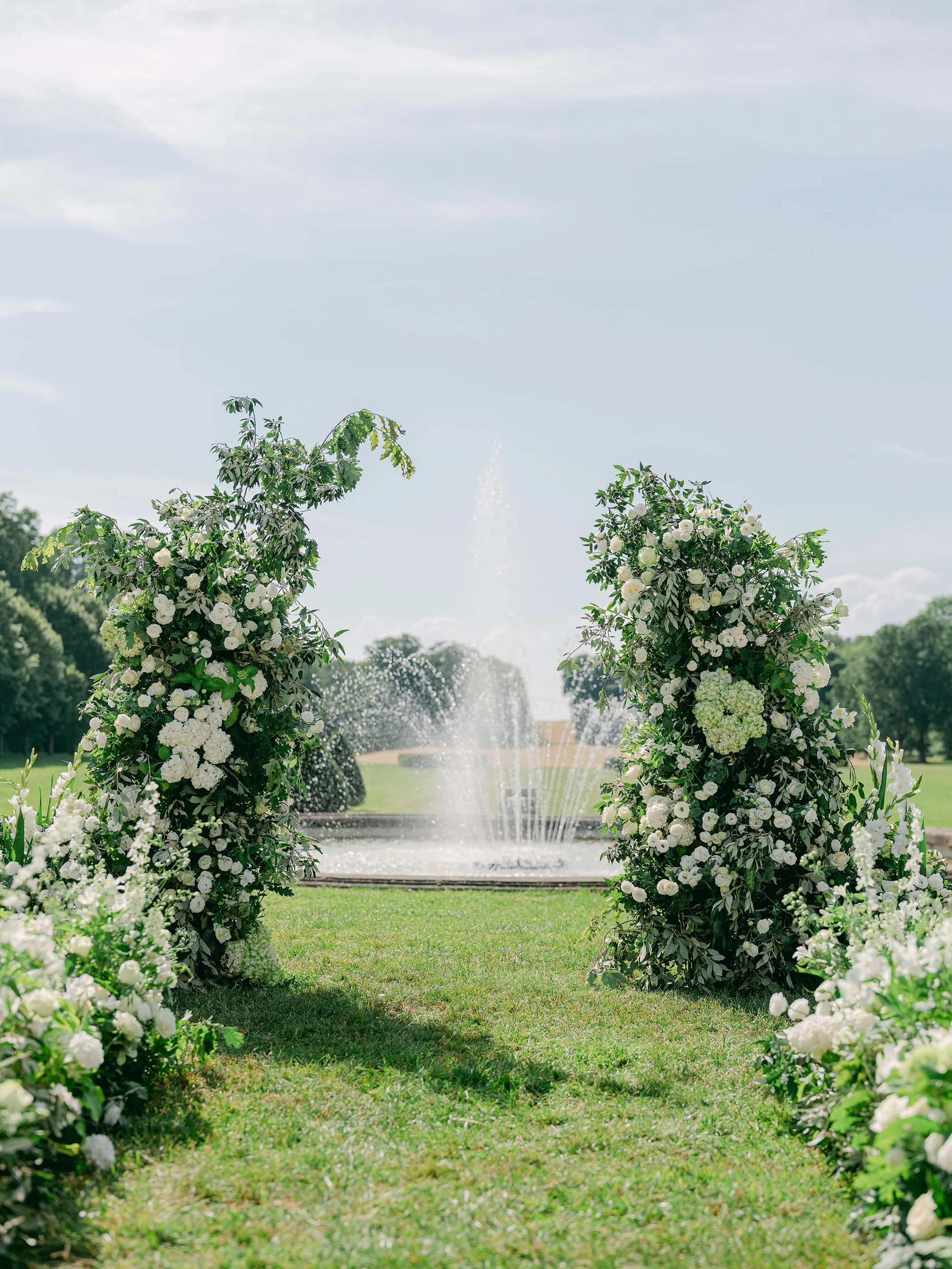 White floral ceremony installations framing the fountain at Château de Champlâtreux
