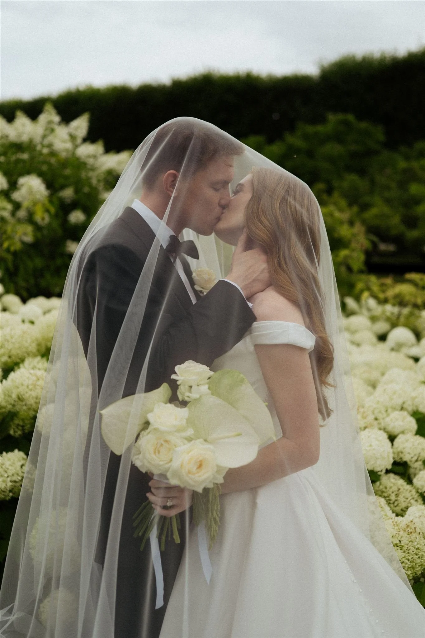 Romantic wedding portrait under the veil surrounded by white hydrangeas in the gardens of Château du Grand-Lucé.