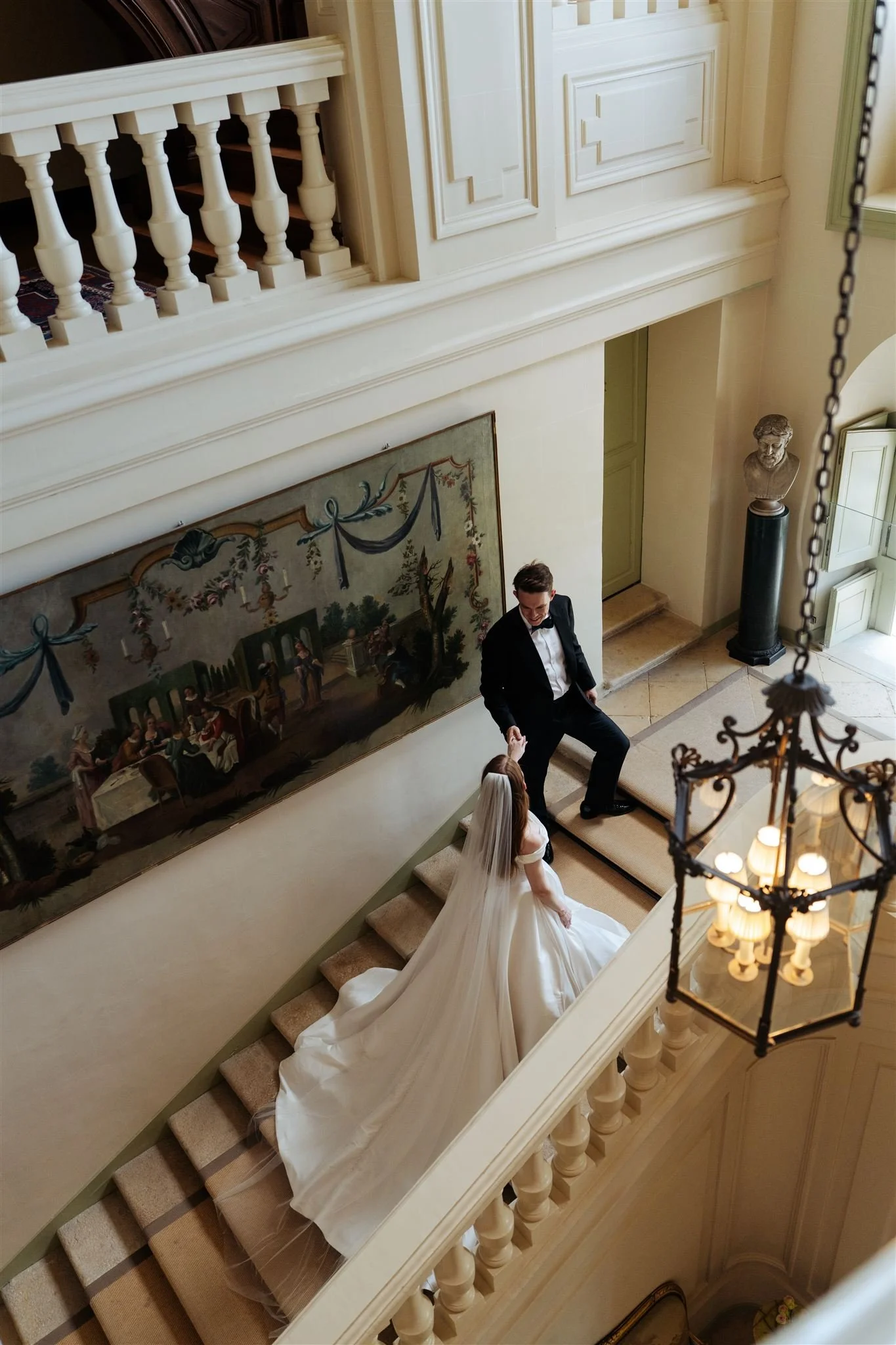 Bride and groom on the grand staircase of Château du Grand-Lucé, surrounded by neoclassical architecture and soft natural light.