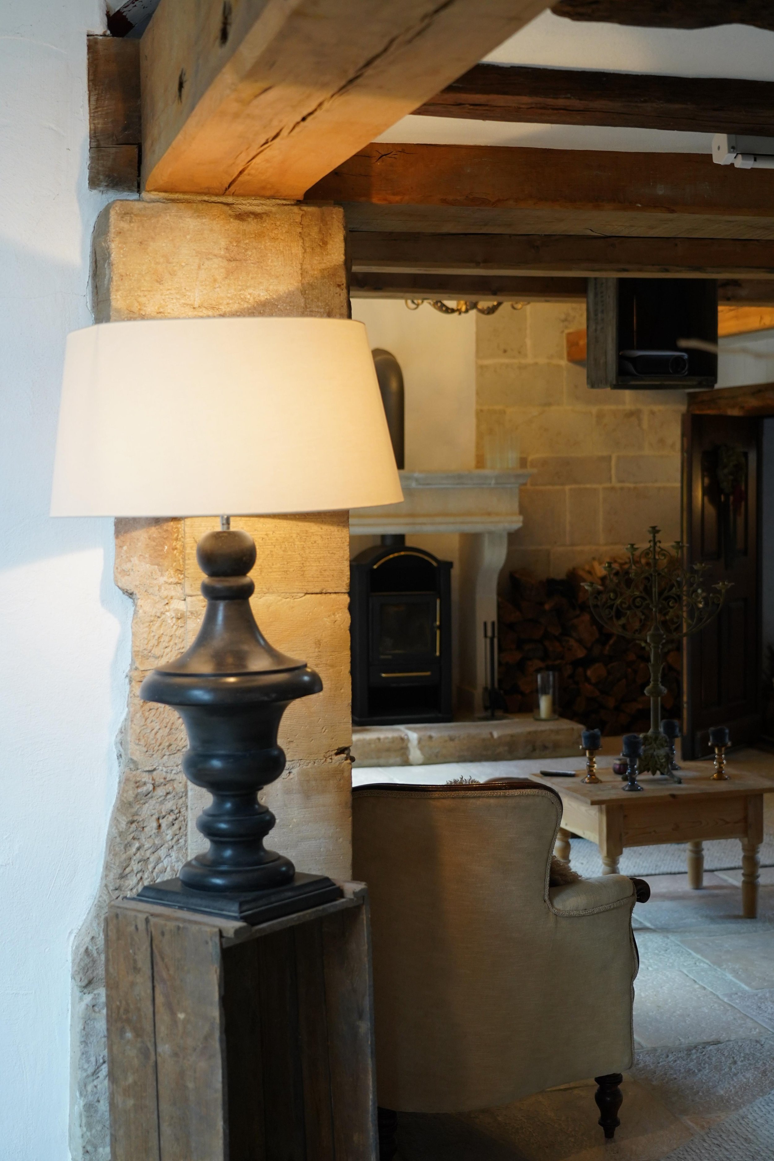 Ein gemütliches Wohnzimmer mit einem schwarzen Stehlampe, einem beigen Sessel, einem Holztisch, einem Kamin und einem Holzofen im Kaminbereich.